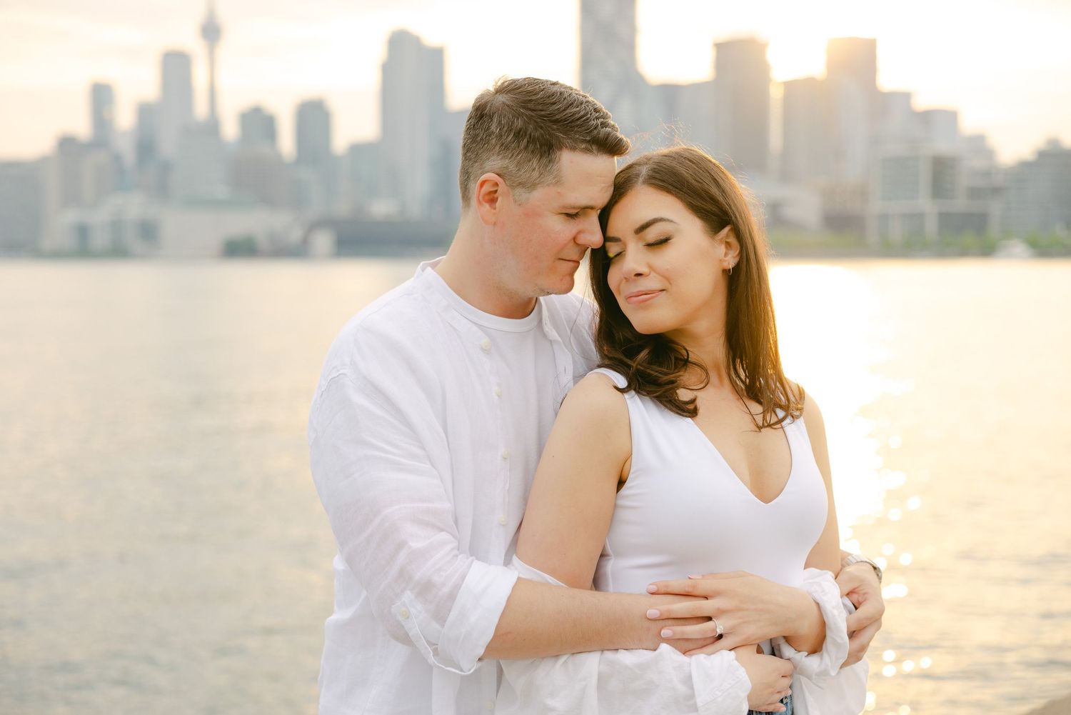Romantic engagement photo with Toronto's spectacular waterfront skyline in soft evening light.