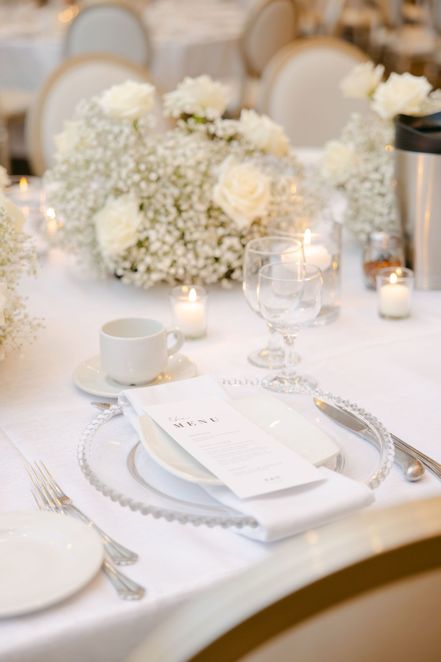 Elegant white wedding table setting with delicate baby's breath centerpiece and glowing candles on a pristine tablecloth.