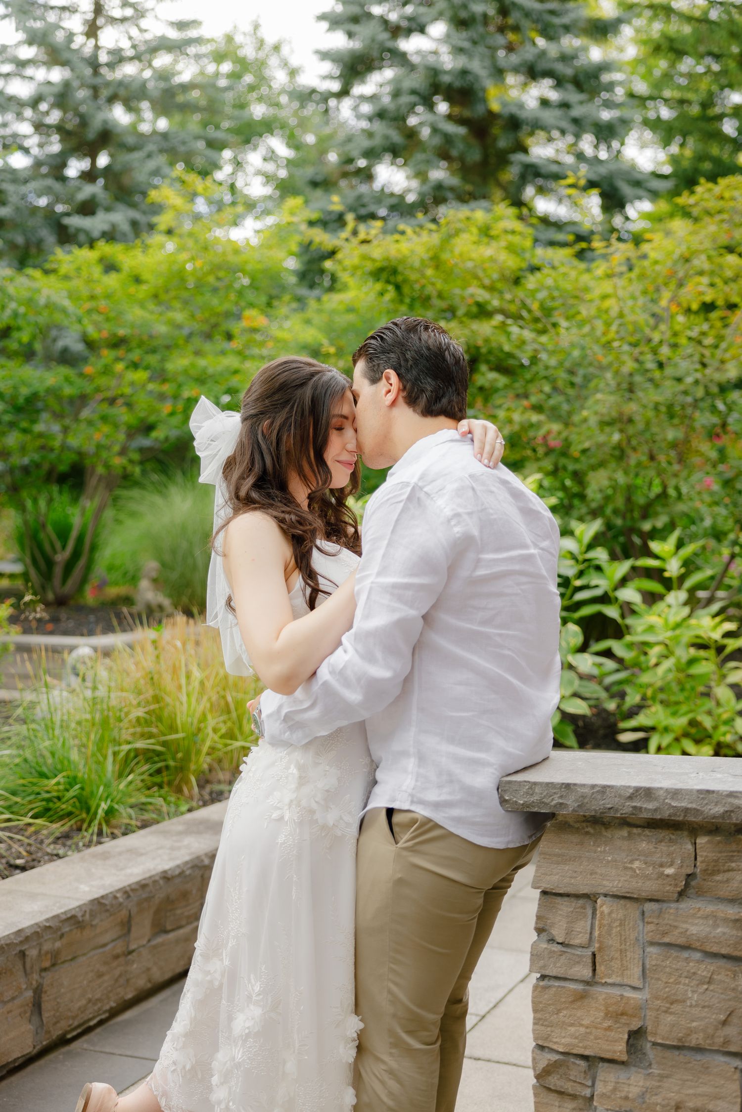 Newlyweds share a romantic moment against a backdrop of vibrant green garden foliage.