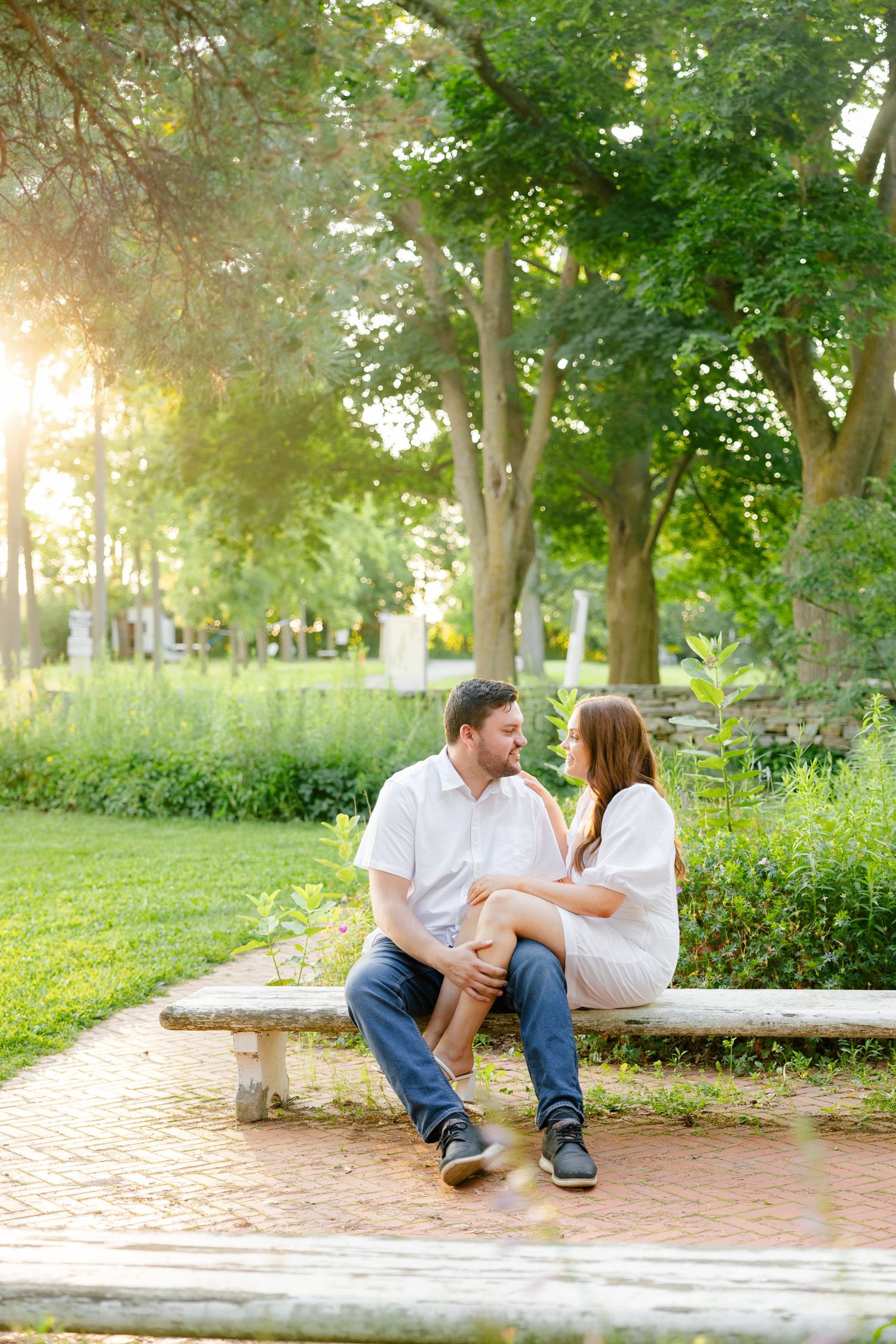 A couple enjoying a romantic moment on a stone bench along a brick pathway at sunset.
