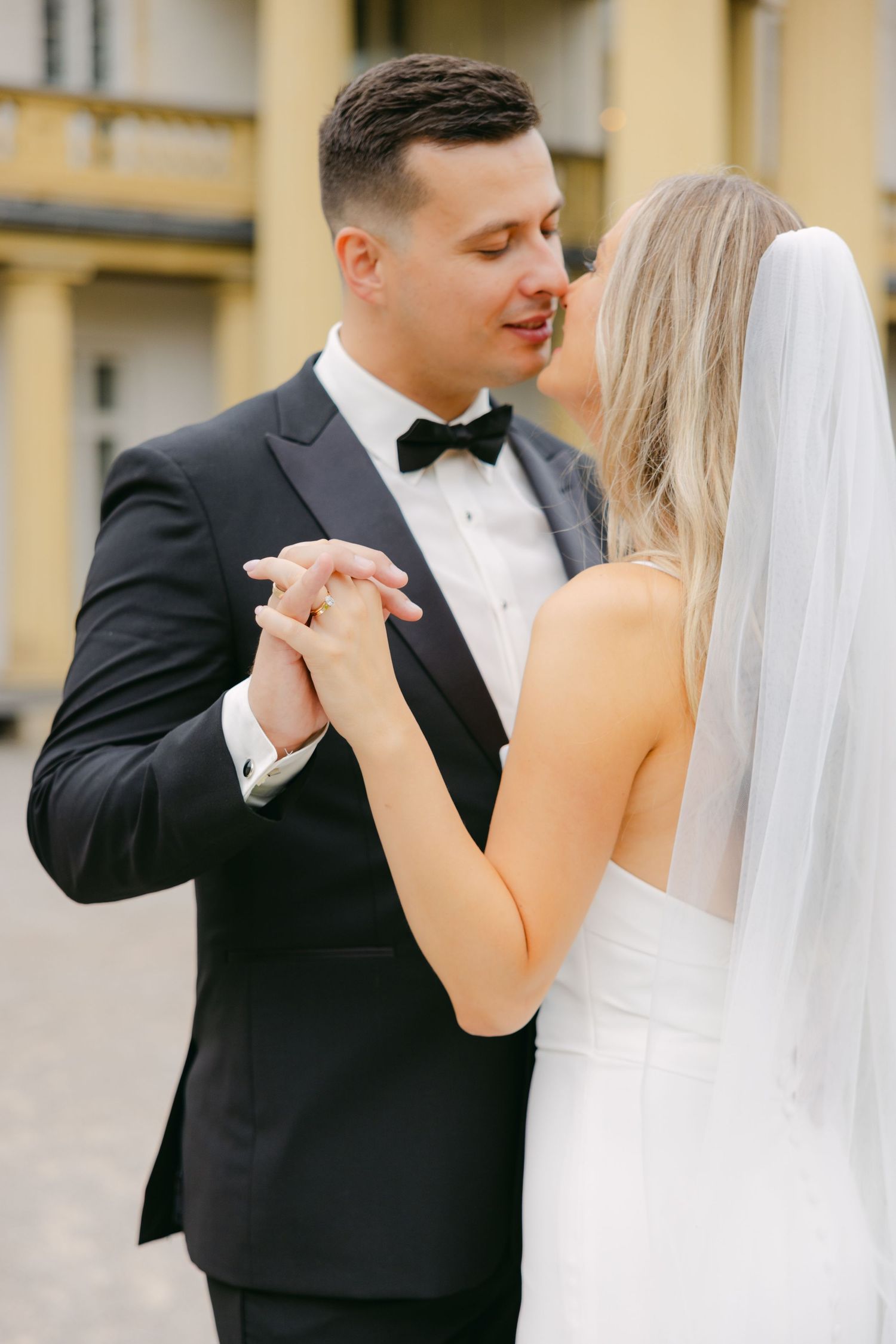 Romantic dance pose of couple in wedding attire against historic building.