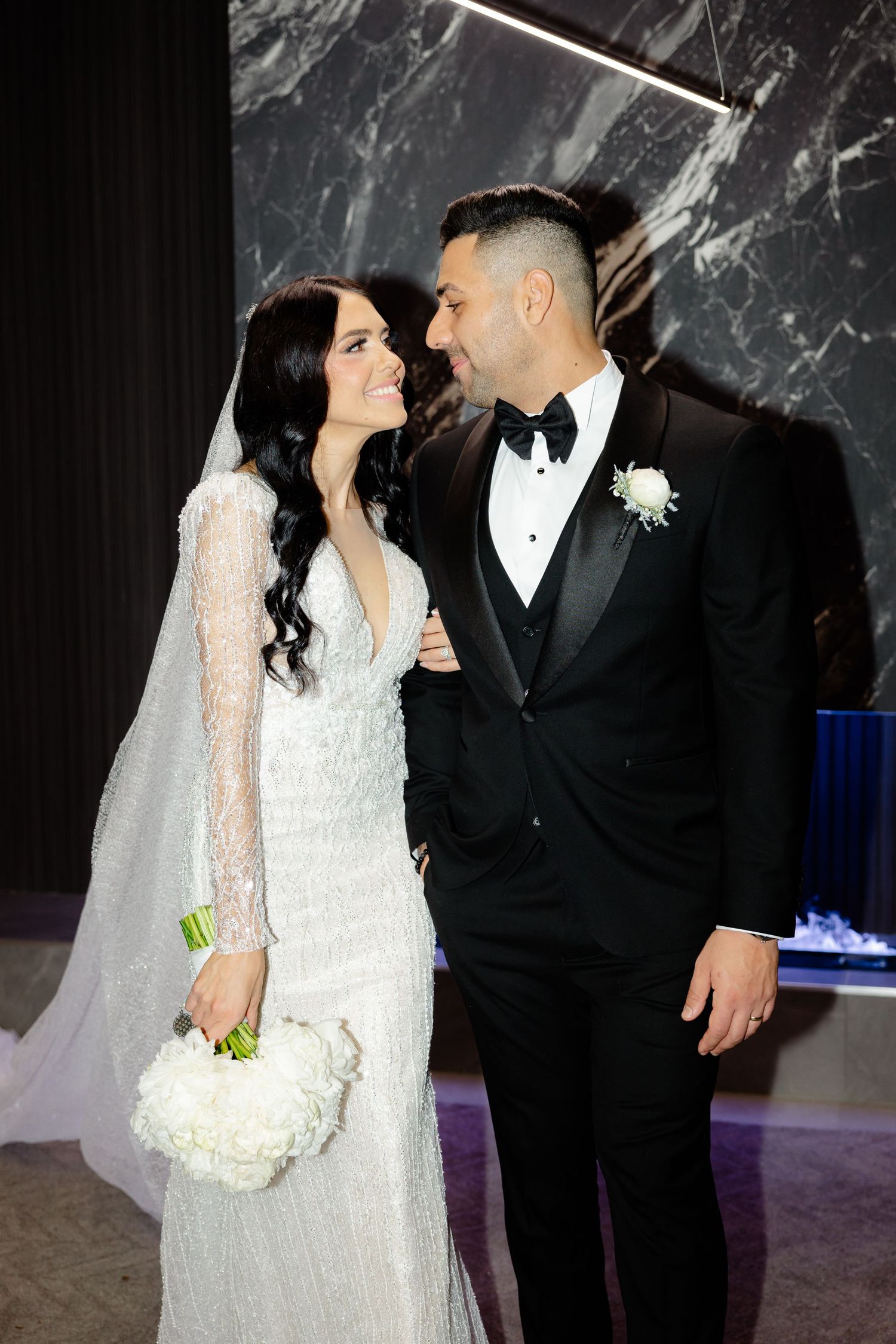 Beautiful wedding portrait with bride holding white bouquet against luxurious marble backdrop.