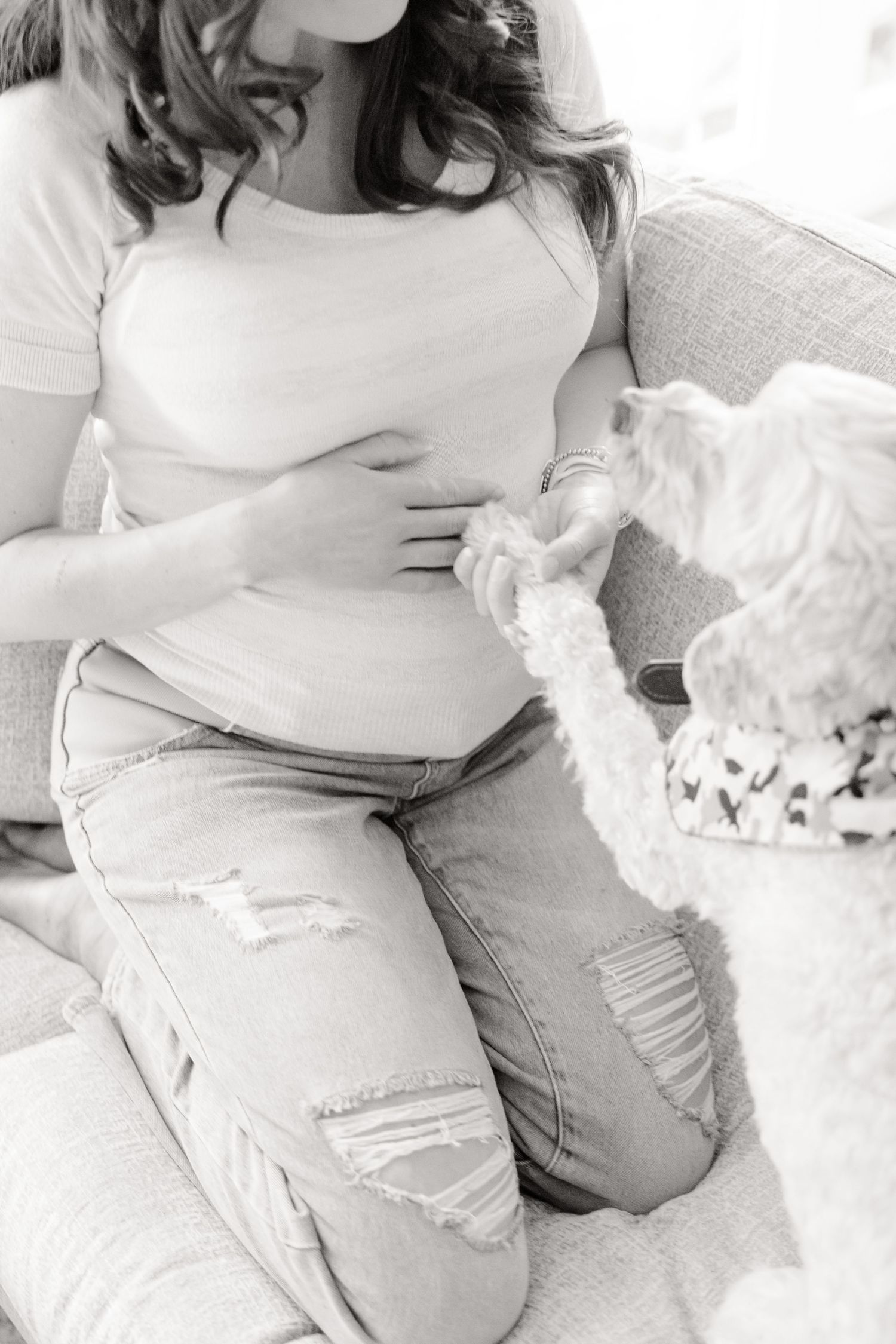 Black and white image of a person in ripped jeans sitting on a couch with a small dog on their lap.
