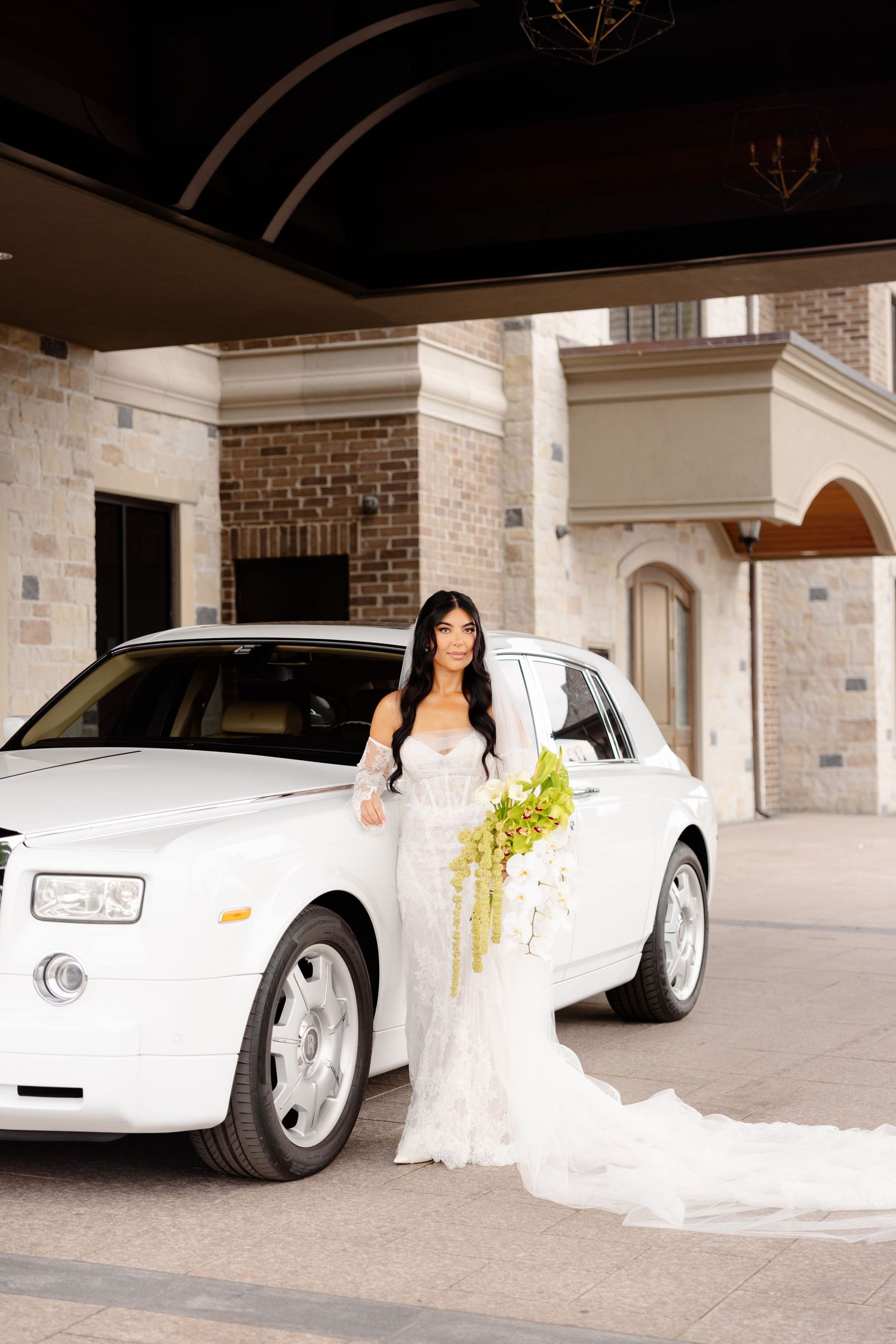 A white wedding dress is elegantly posed next to a sleek white luxury car in a covered parking area.