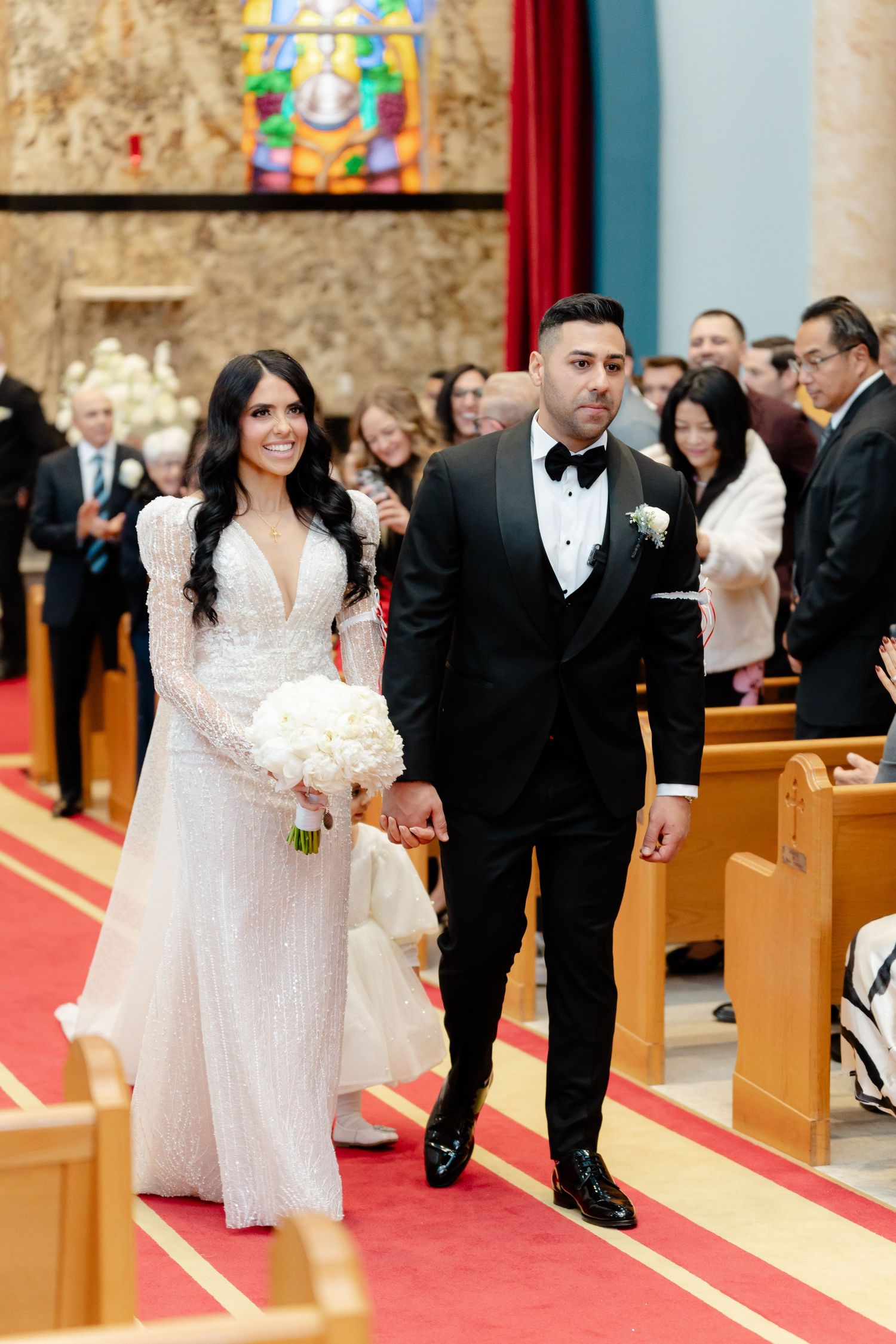 A couple walks down the red-carpeted aisle of a church after their wedding ceremony.