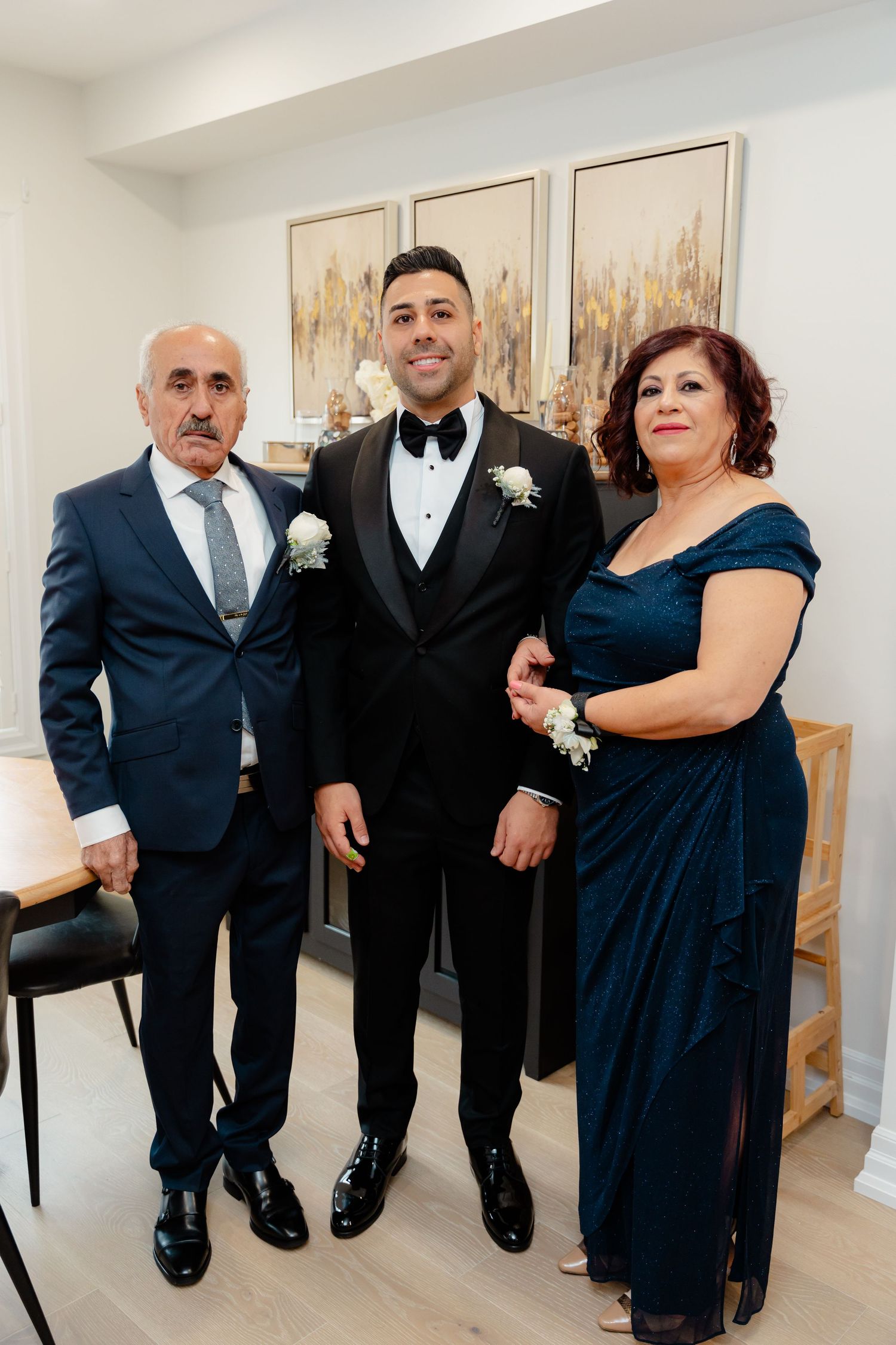 Three family members pose together in formal evening wear against neutral wall art.