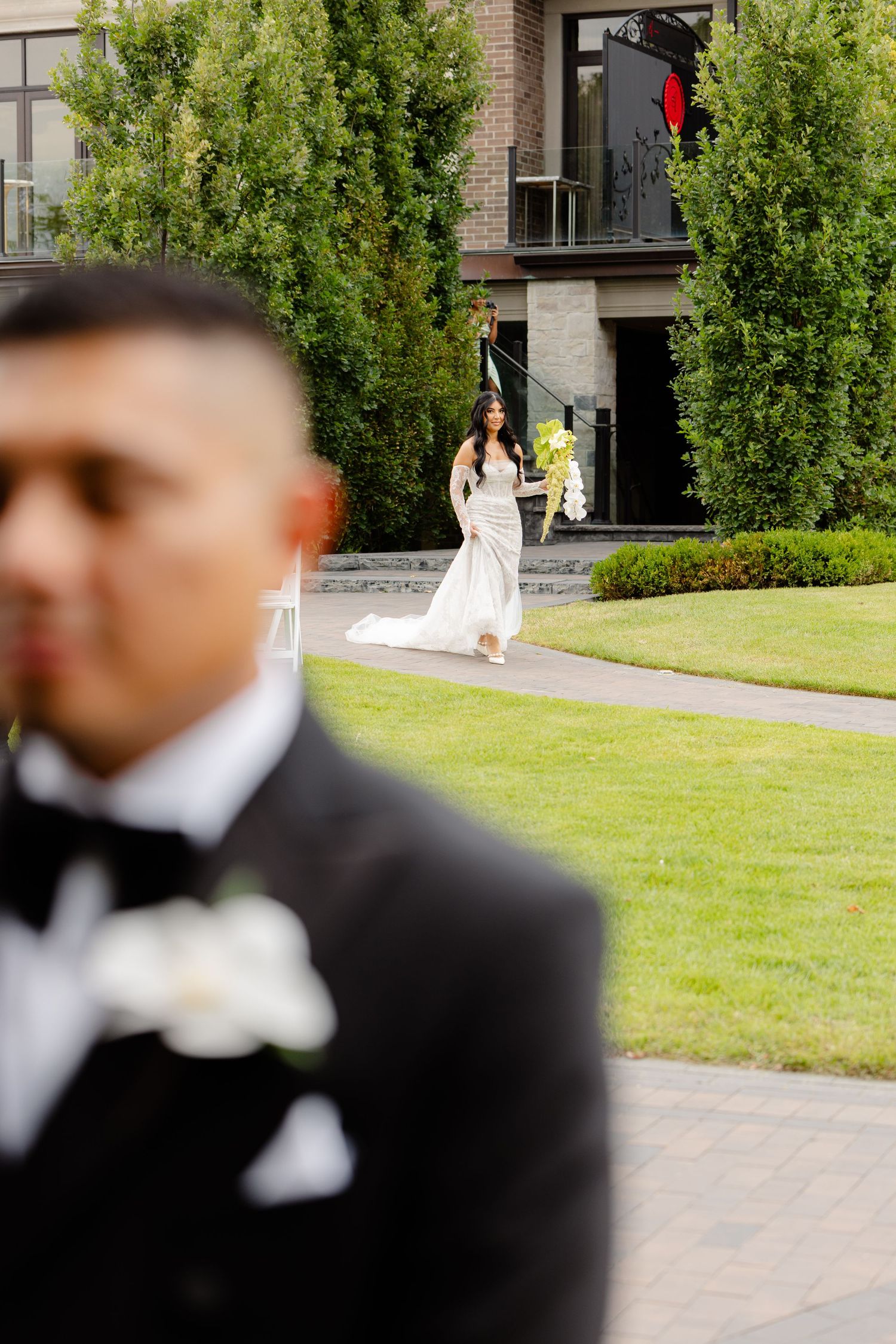 Wedding couple shares intimate first look moment on a grassy lawn in front of a brick building.