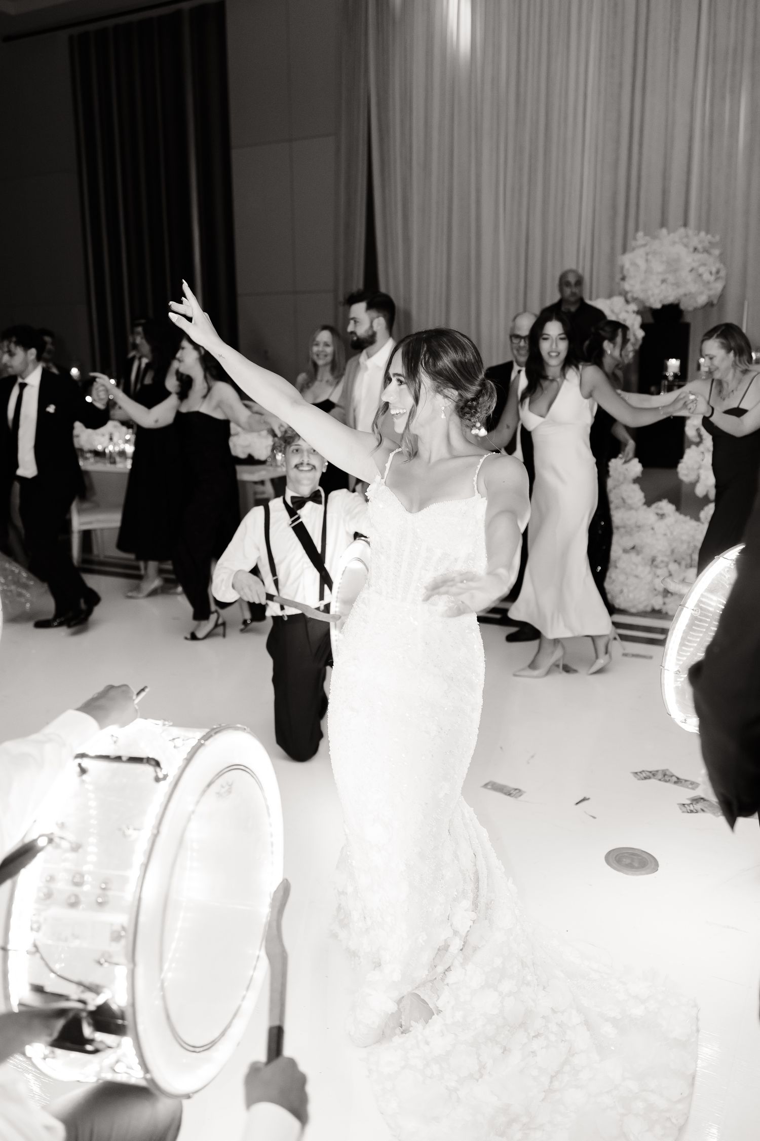 A bride in a white dress dances with her arms raised during a wedding reception celebration.