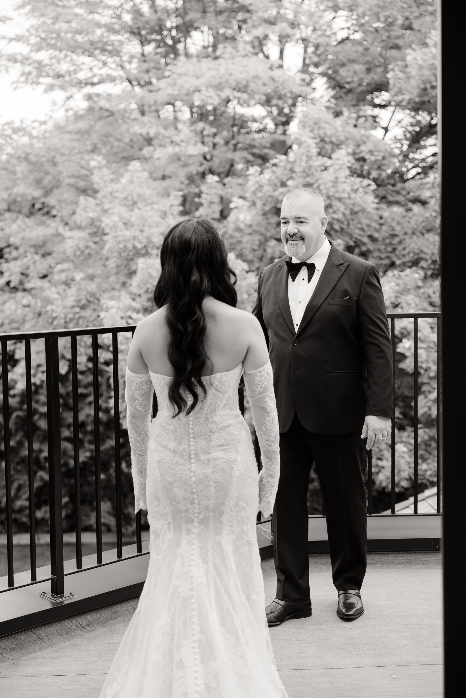 A touching first look wedding moment captured in a series of black and white photos on an outdoor deck overlooking trees.