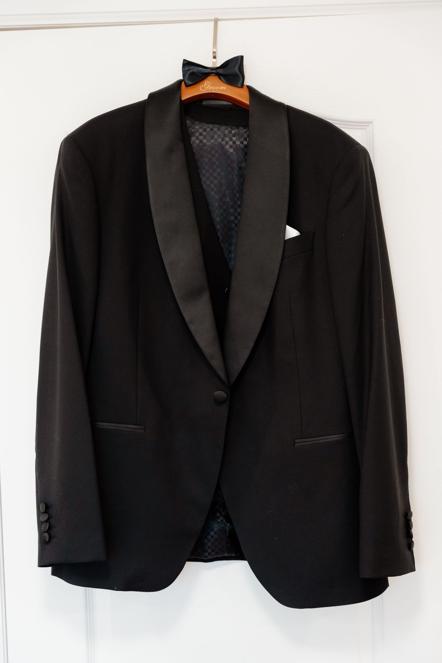 Classic black tuxedo jacket with shawl collar hanging on wooden hanger.