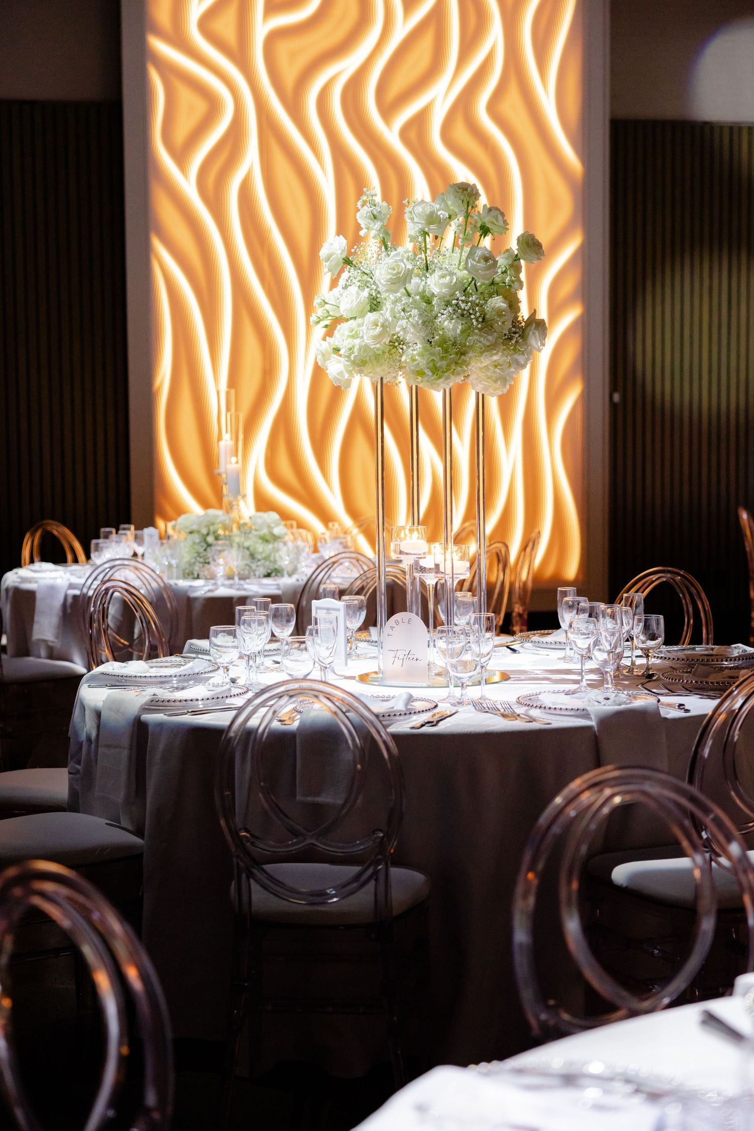 Modern reception venue with illuminated orange wave pattern wall and ghost chairs.