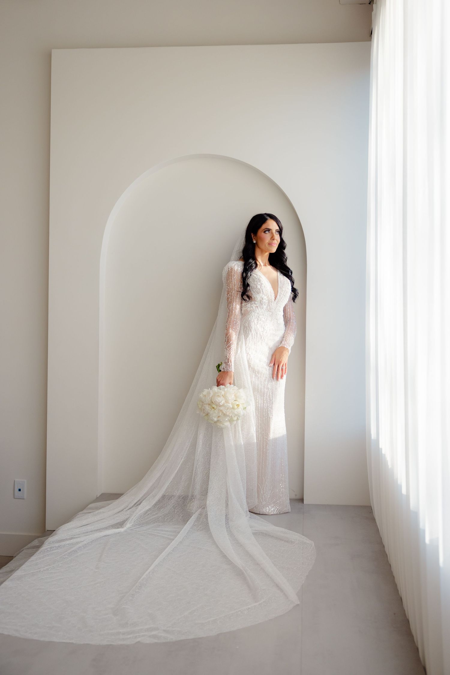 Elegant bridal portrait in arched doorway featuring long flowing veil and white bouquet.