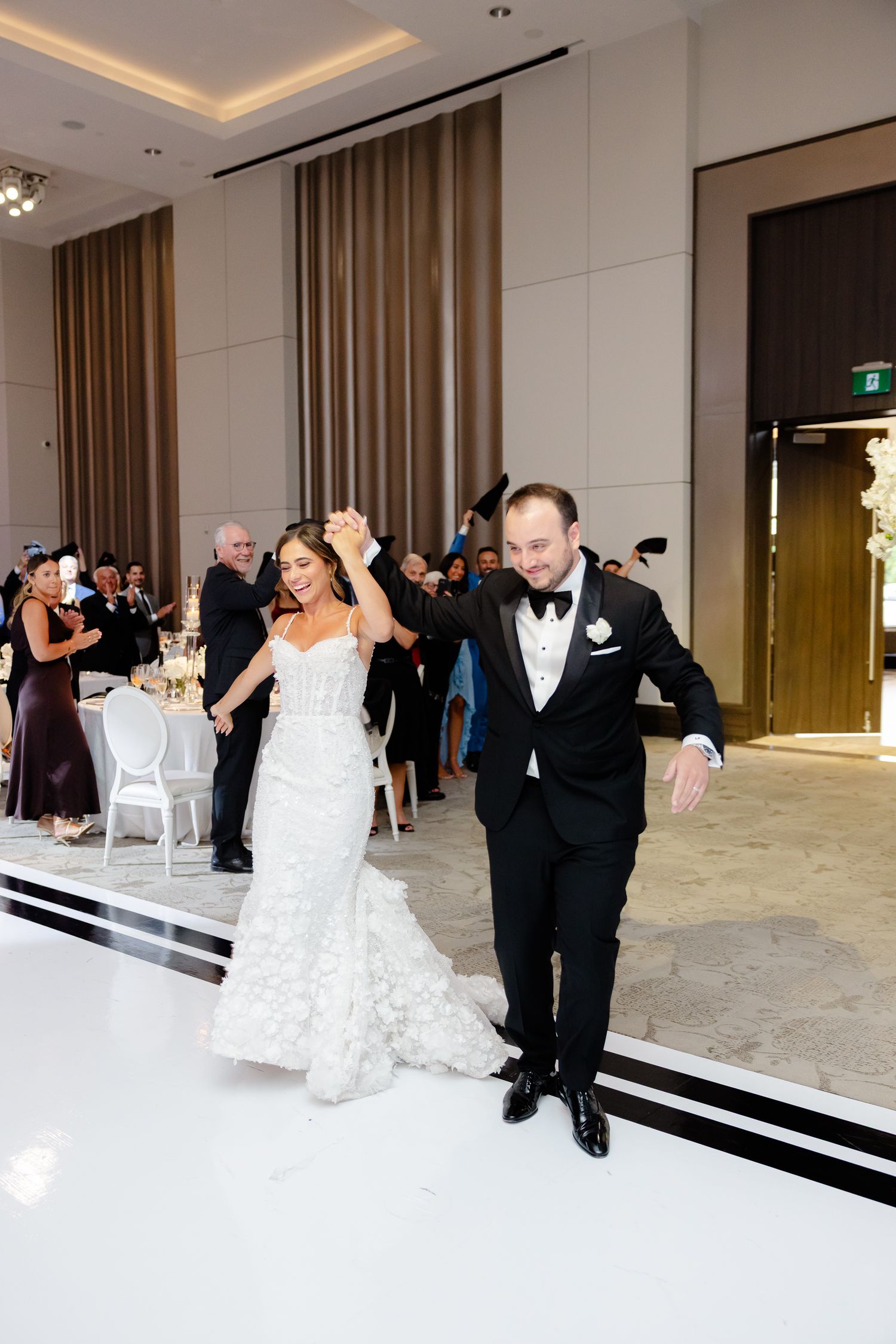 A couple shares their first dance together at their wedding reception in an elegant white ballroom setting.