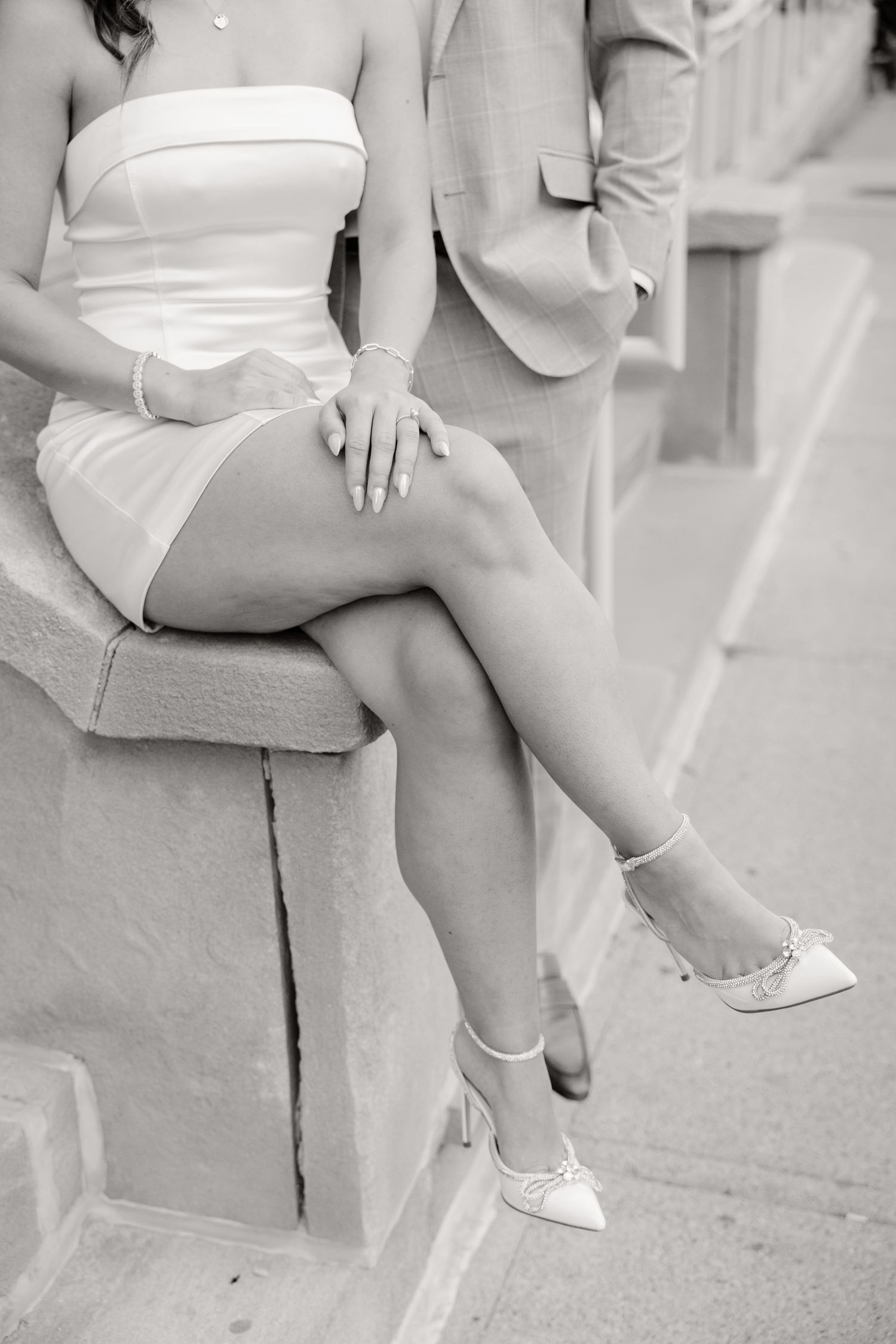 Black and white photo showing elegant dress and heels detail while seated on stone steps.