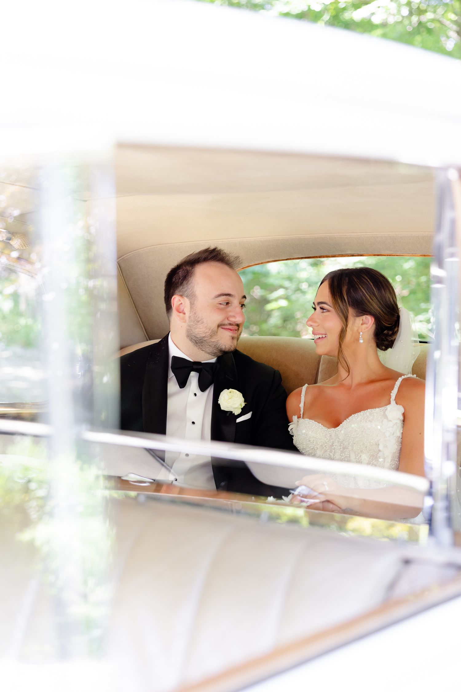 A romantic wedding moment captured through a car window showing a bride and groom in formal attire.