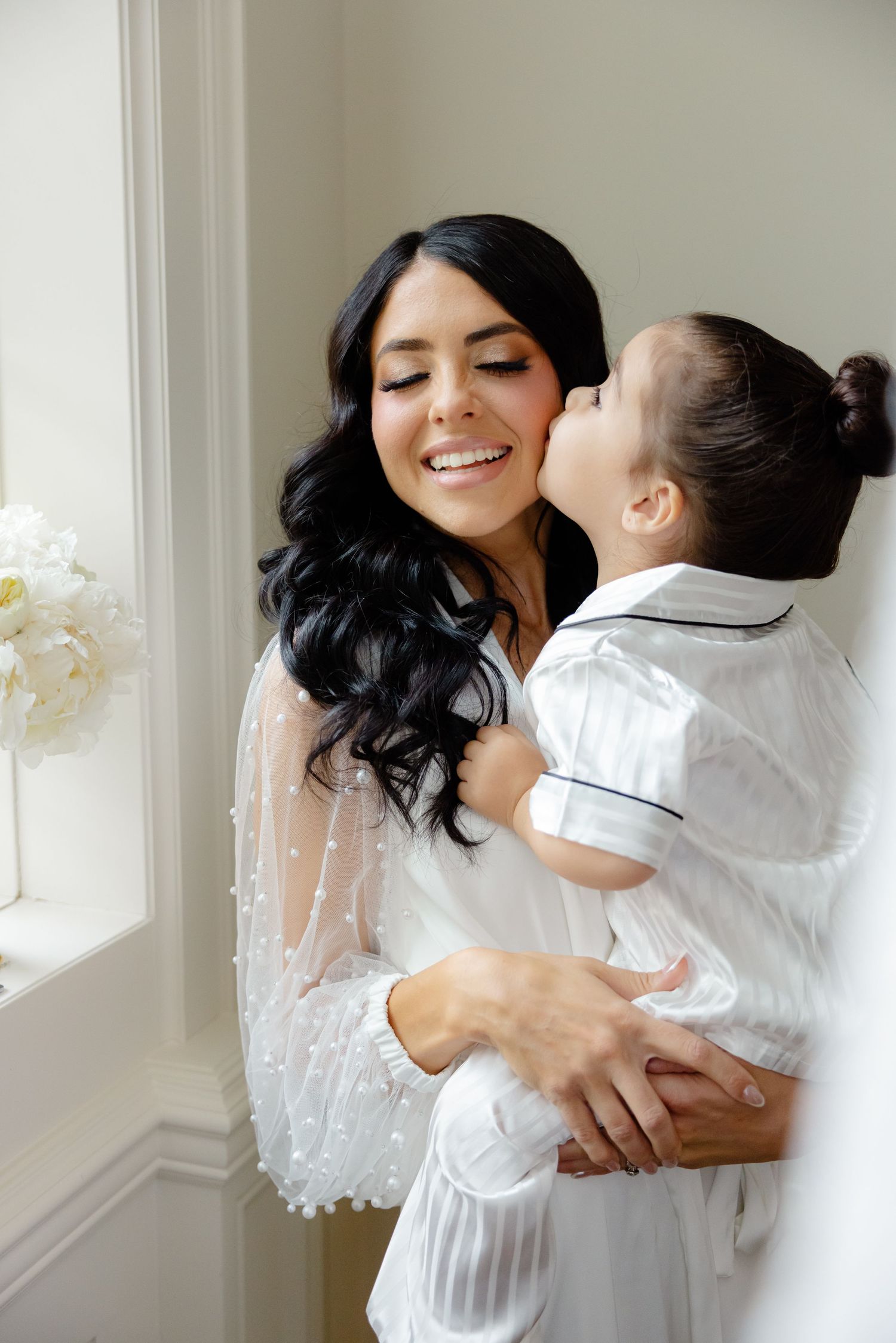 An intimate moment shared between parent and child by a window with white flowers.