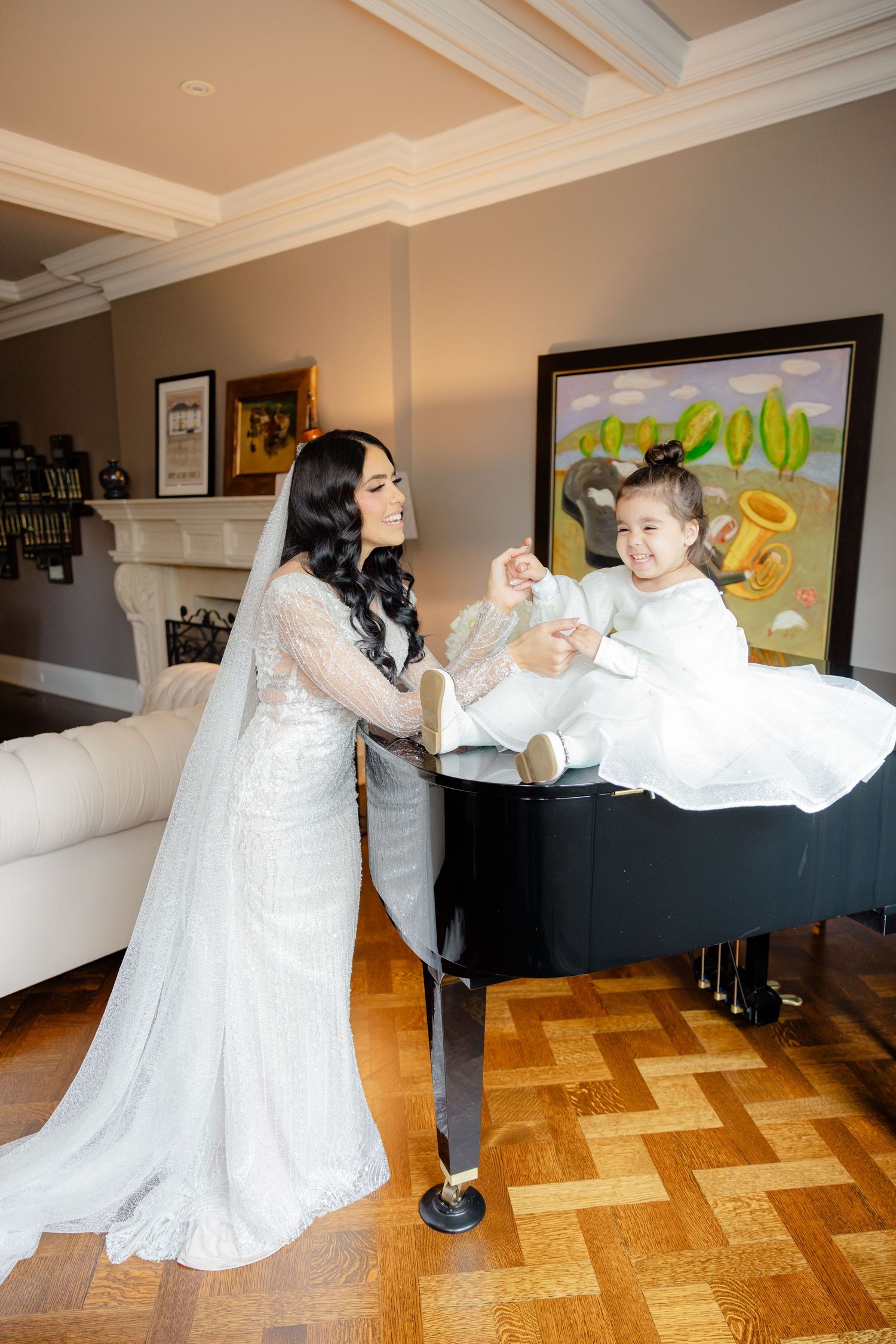 A bride in a lace gown interacts with a young attendant perched on a black piano.