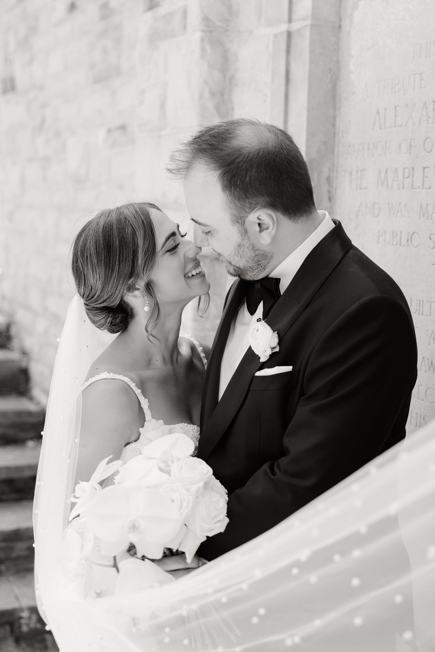 A romantic black and white wedding moment captured as the couple shares an intimate close moment with a white bouquet.