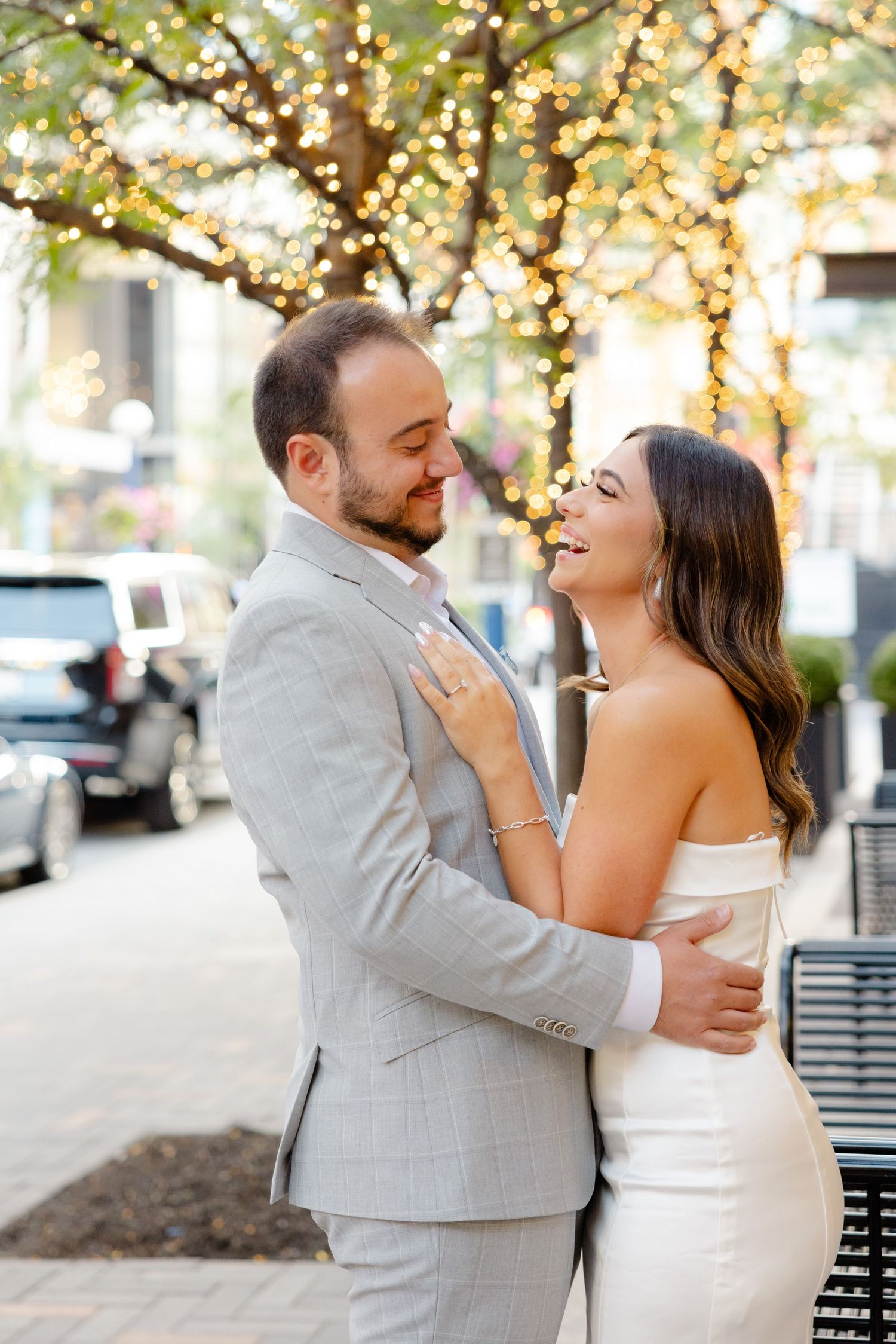 Couple in formal attire shares romantic moment under tree with twinkling lights.