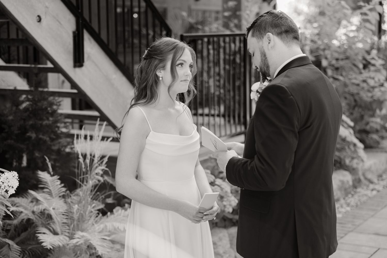 A black and white wedding ceremony moment showing a couple exchanging vows in a garden setting.