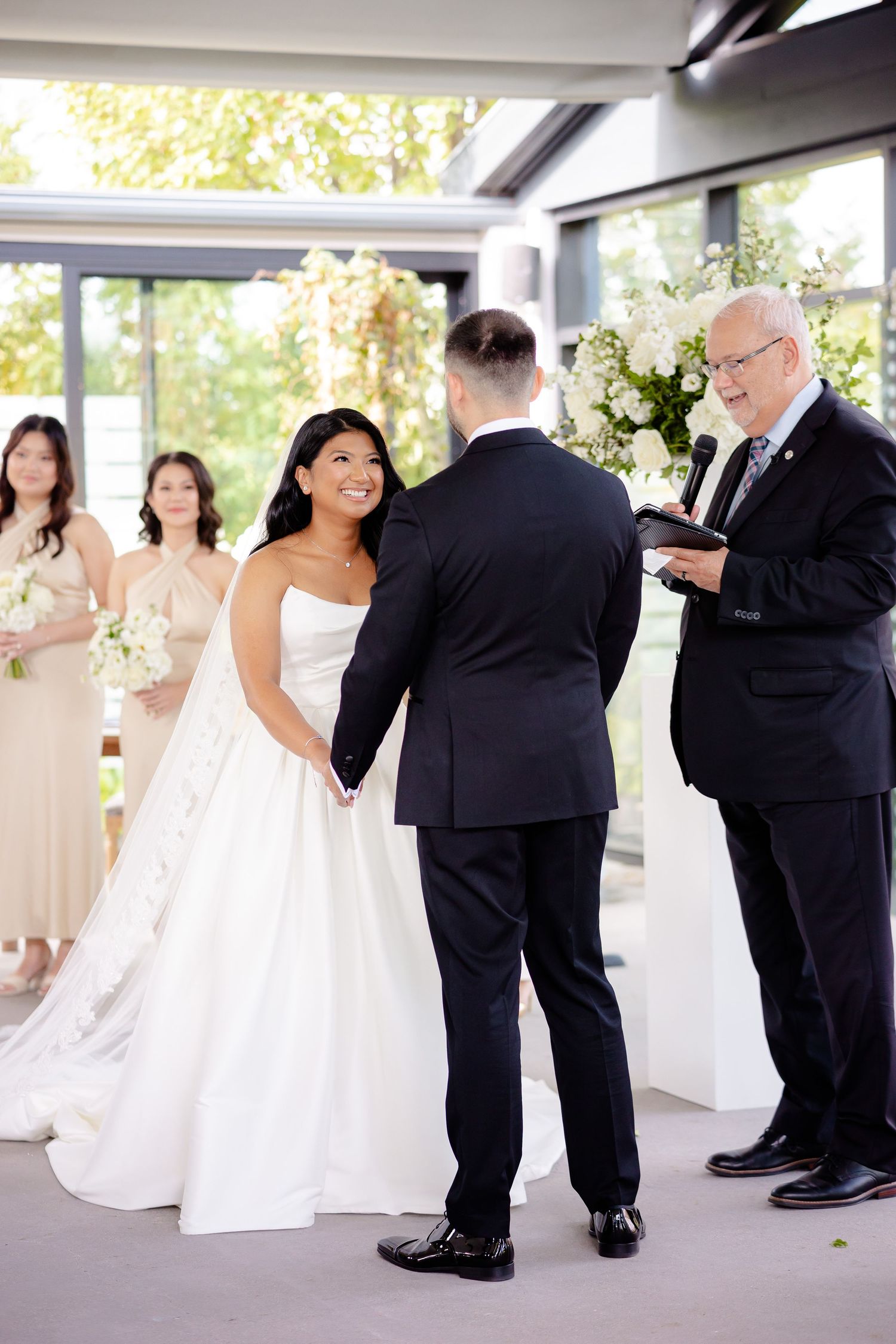 Indoor wedding ceremony with bridesmaids in blush dresses and an officiant conducting the service.