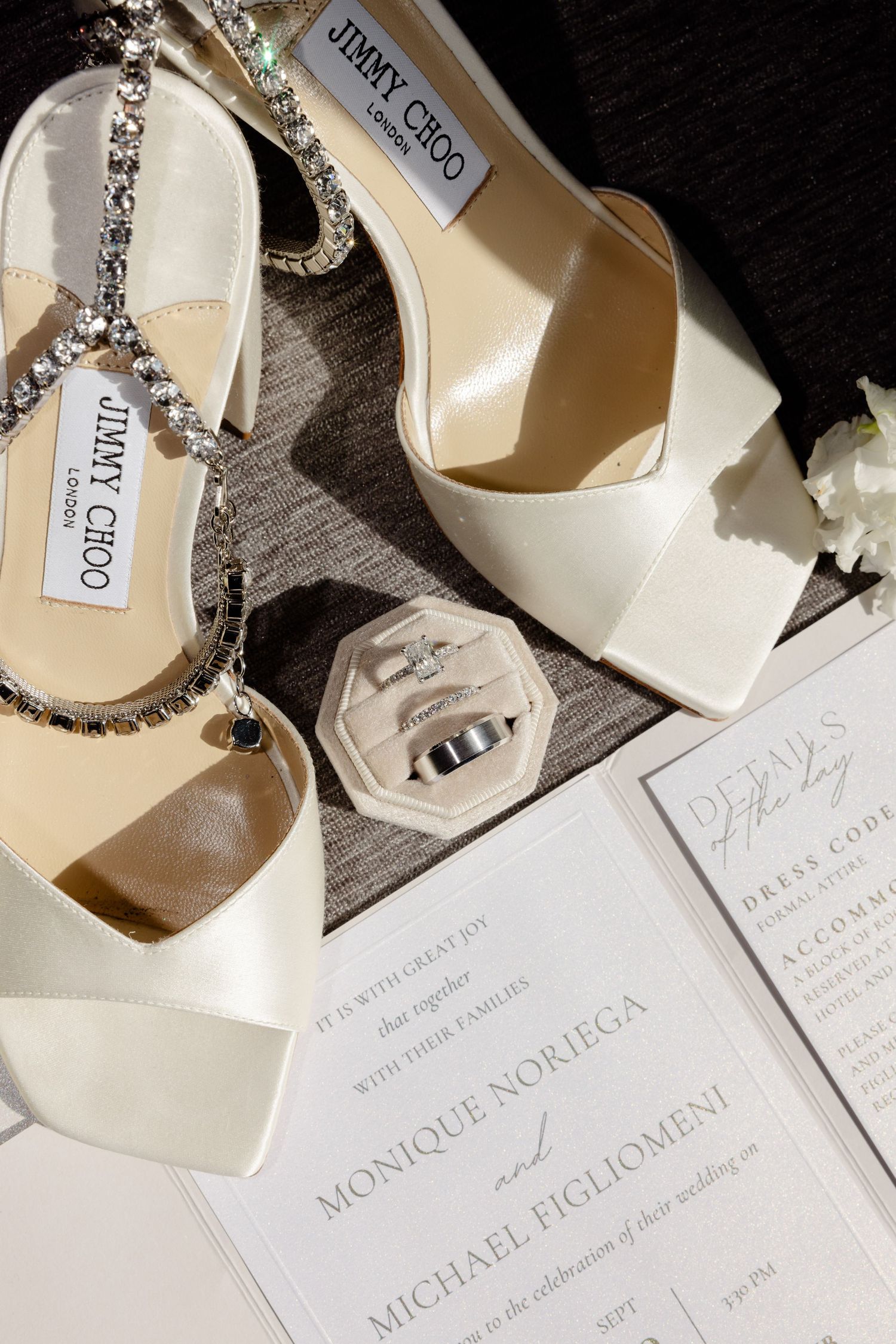 Elegant white Jimmy Choo bridal shoes with crystal straps next to wedding invitation.