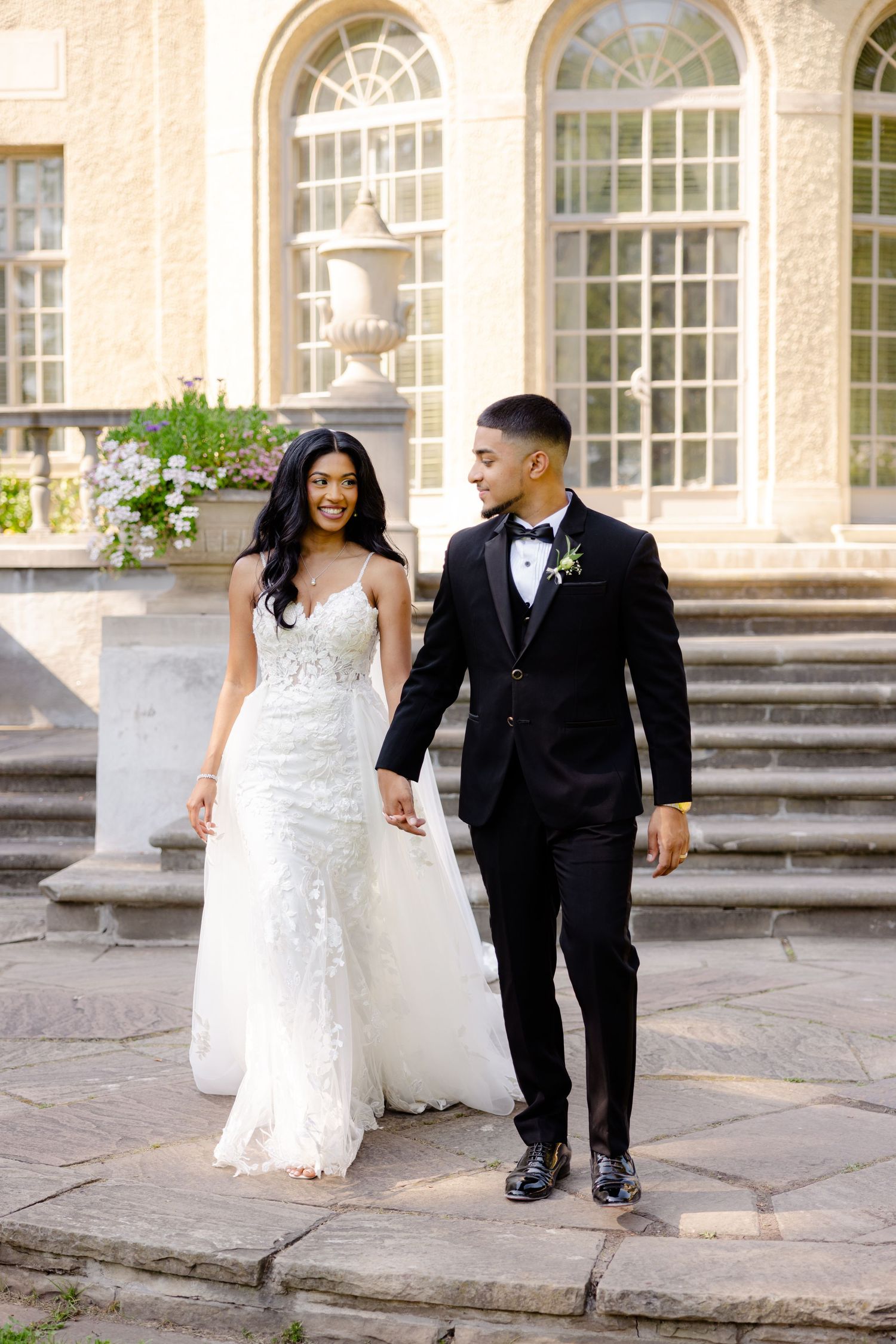 A couple shares a joyful moment at the bottom of stone steps in front of a stately mansion.
