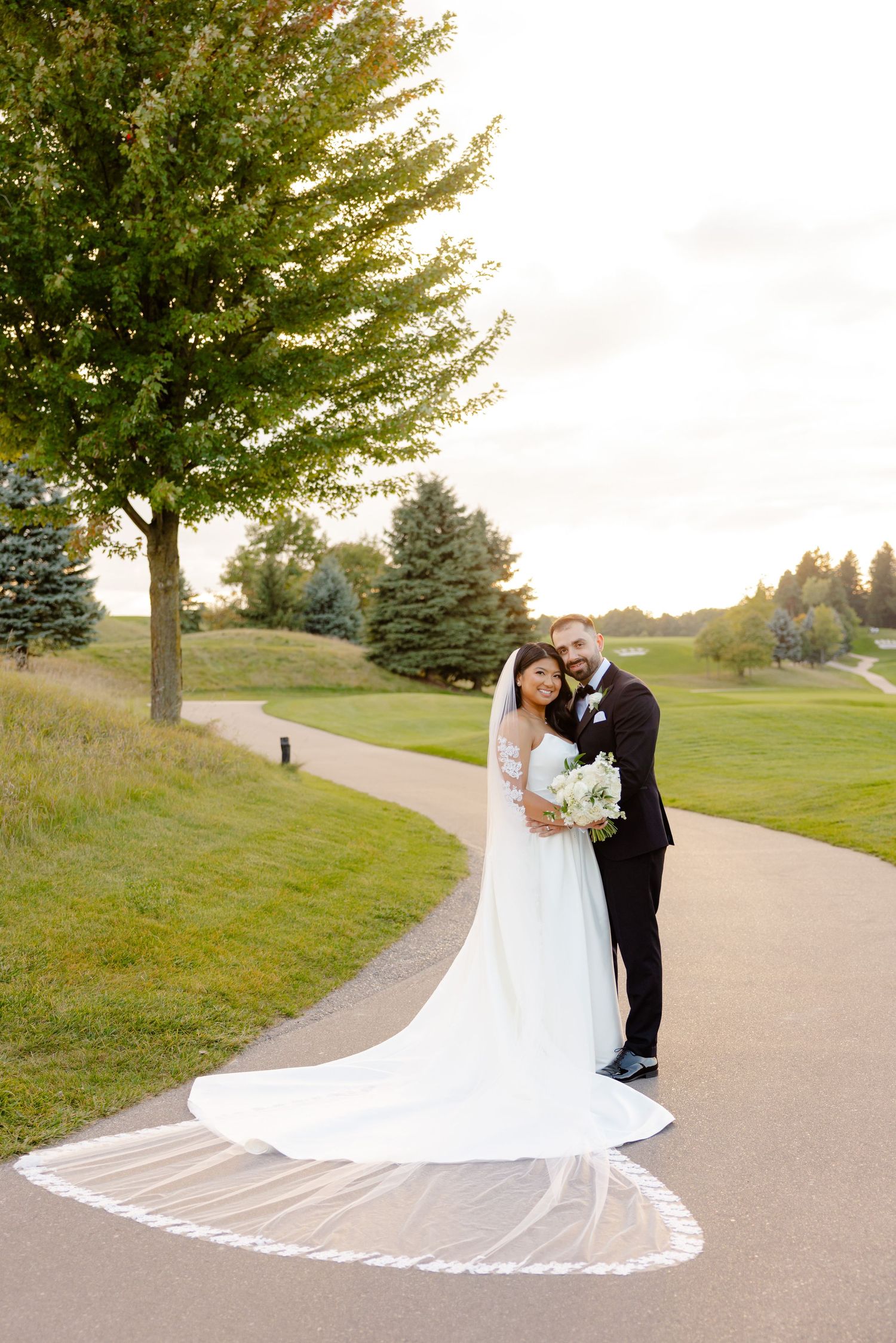 A beautiful wedding photo on a golf course with a flowing cathedral veil in the afternoon light.