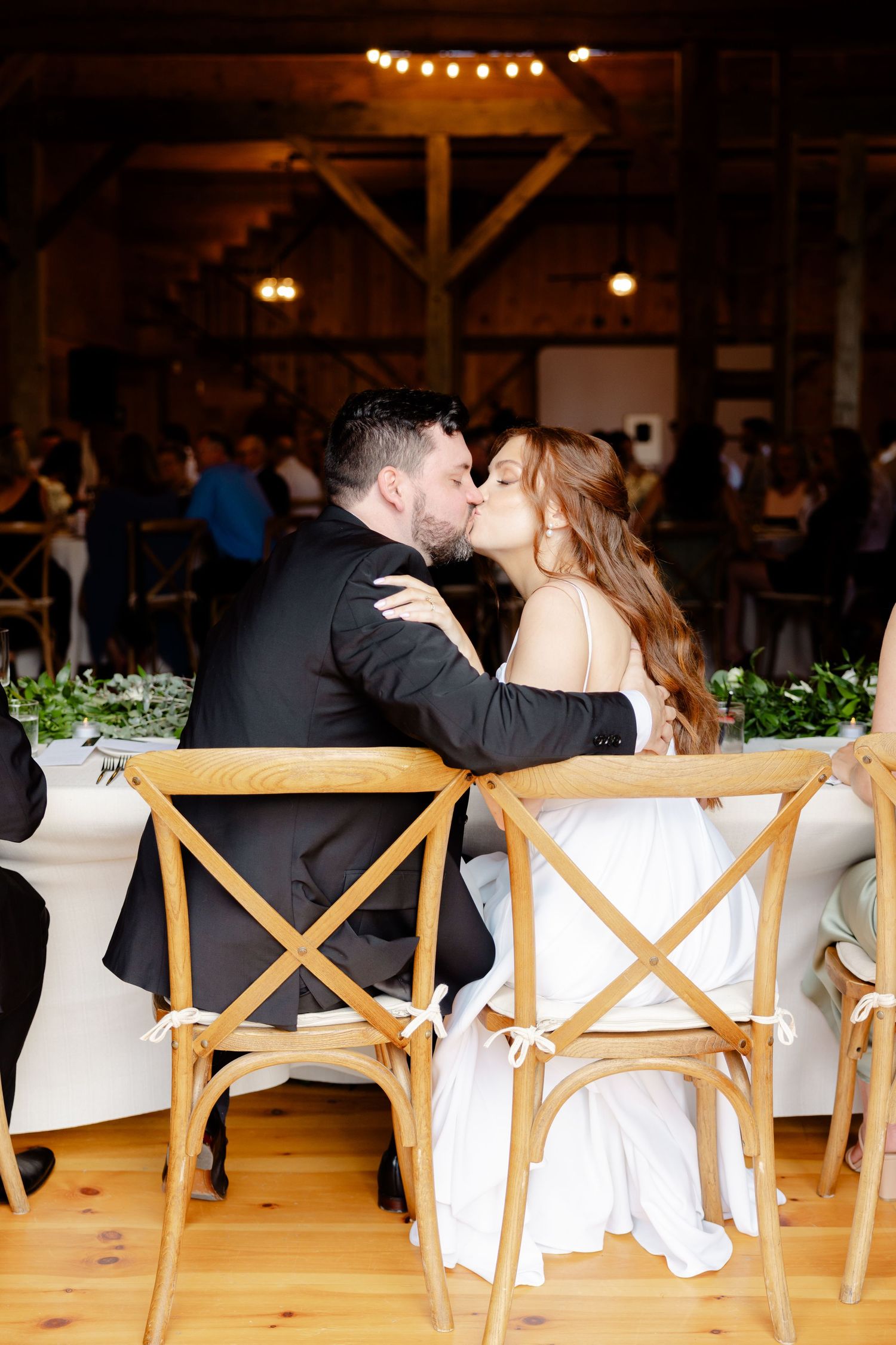 Intimate moment captured during a wedding reception in a rustic barn setting with string lights overhead.