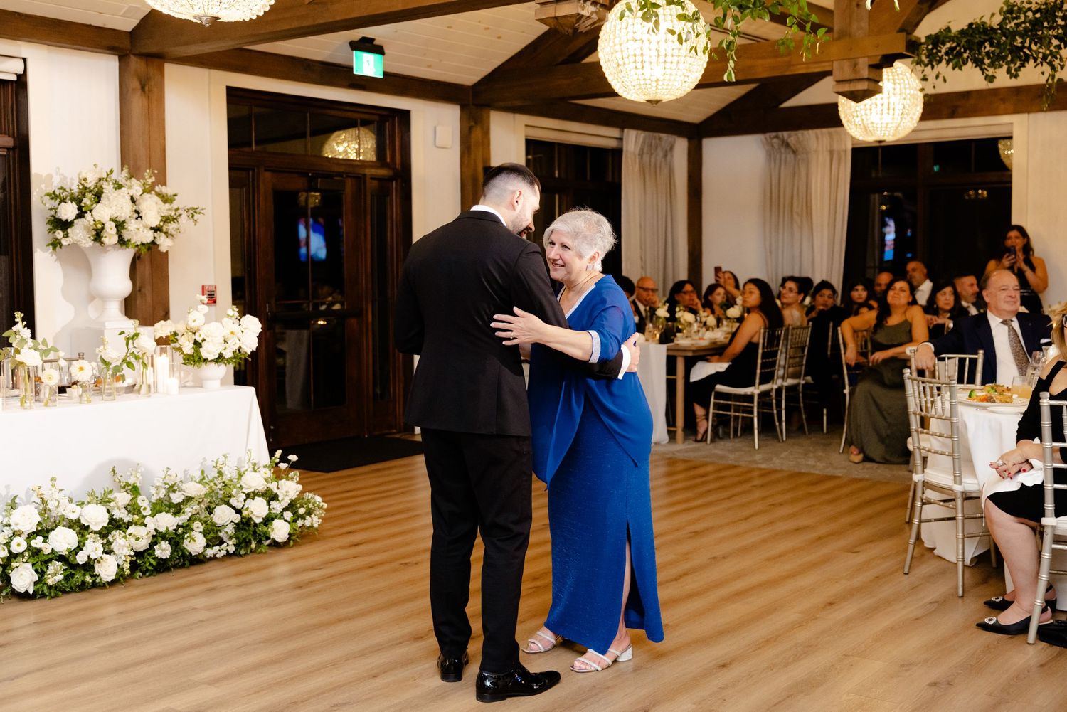 Dance moment in an elegant reception venue with wooden beams and crystal chandeliers.