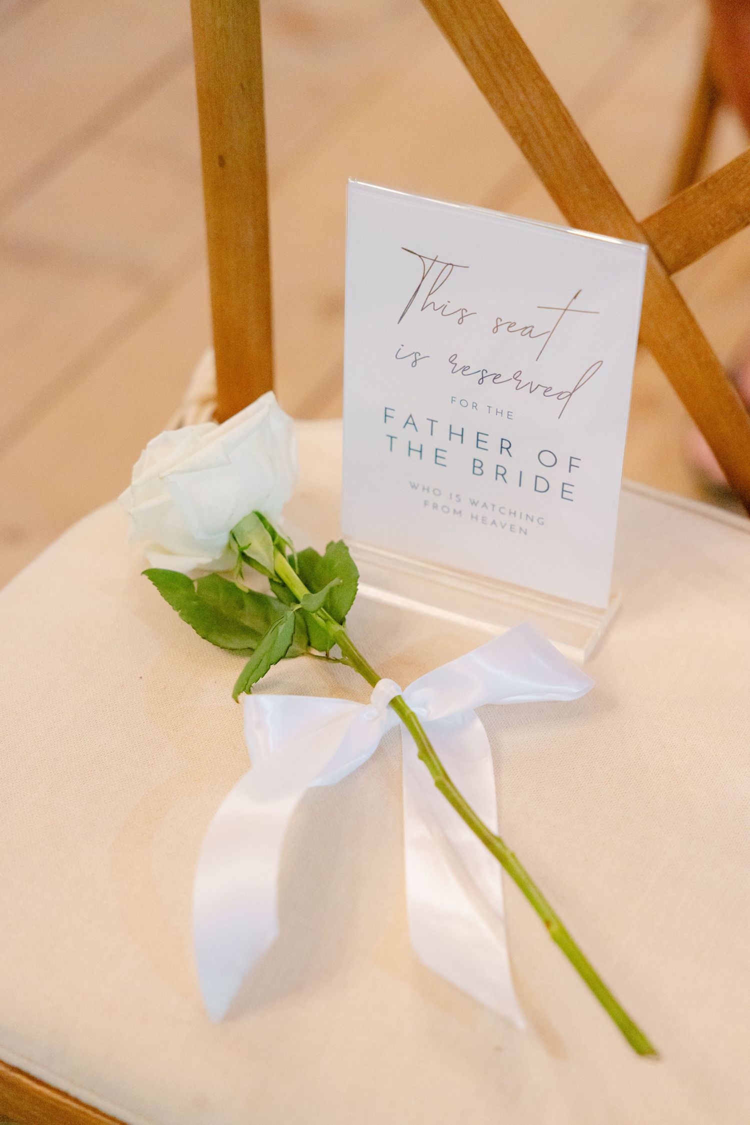 Reserved seating sign for Father of the Bride with a white rose and ribbon on a wooden chair.