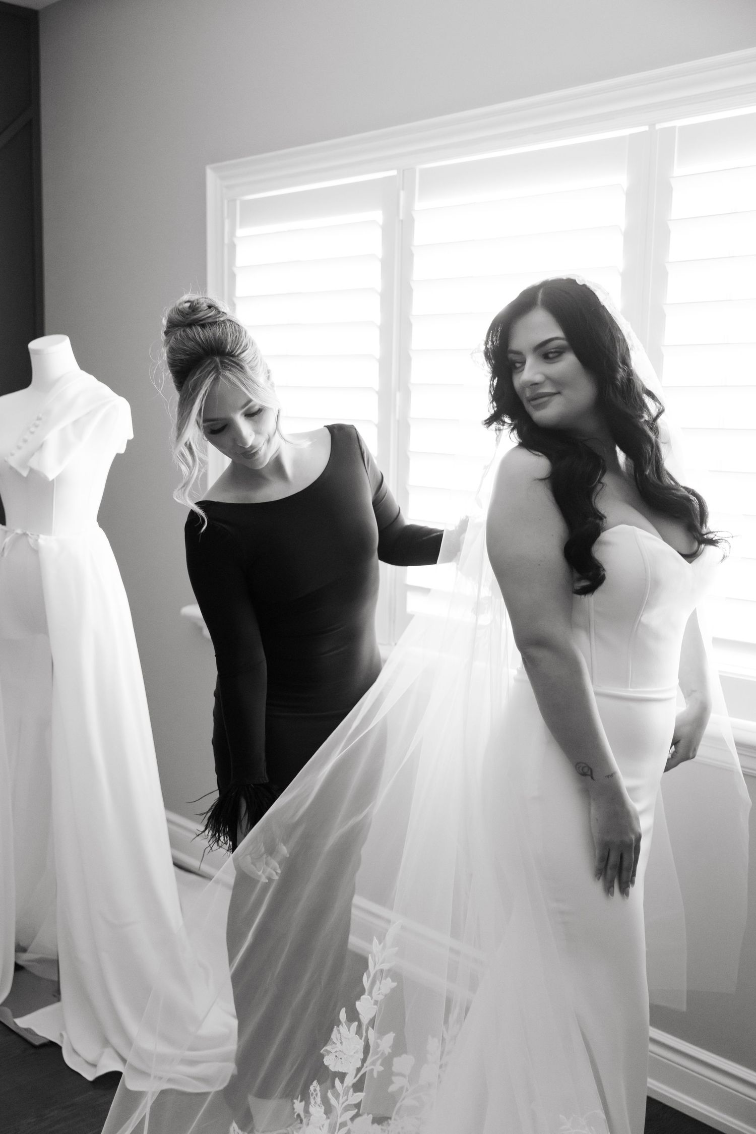 Black and white image of bridal preparations with dress form and flowing white gown.
