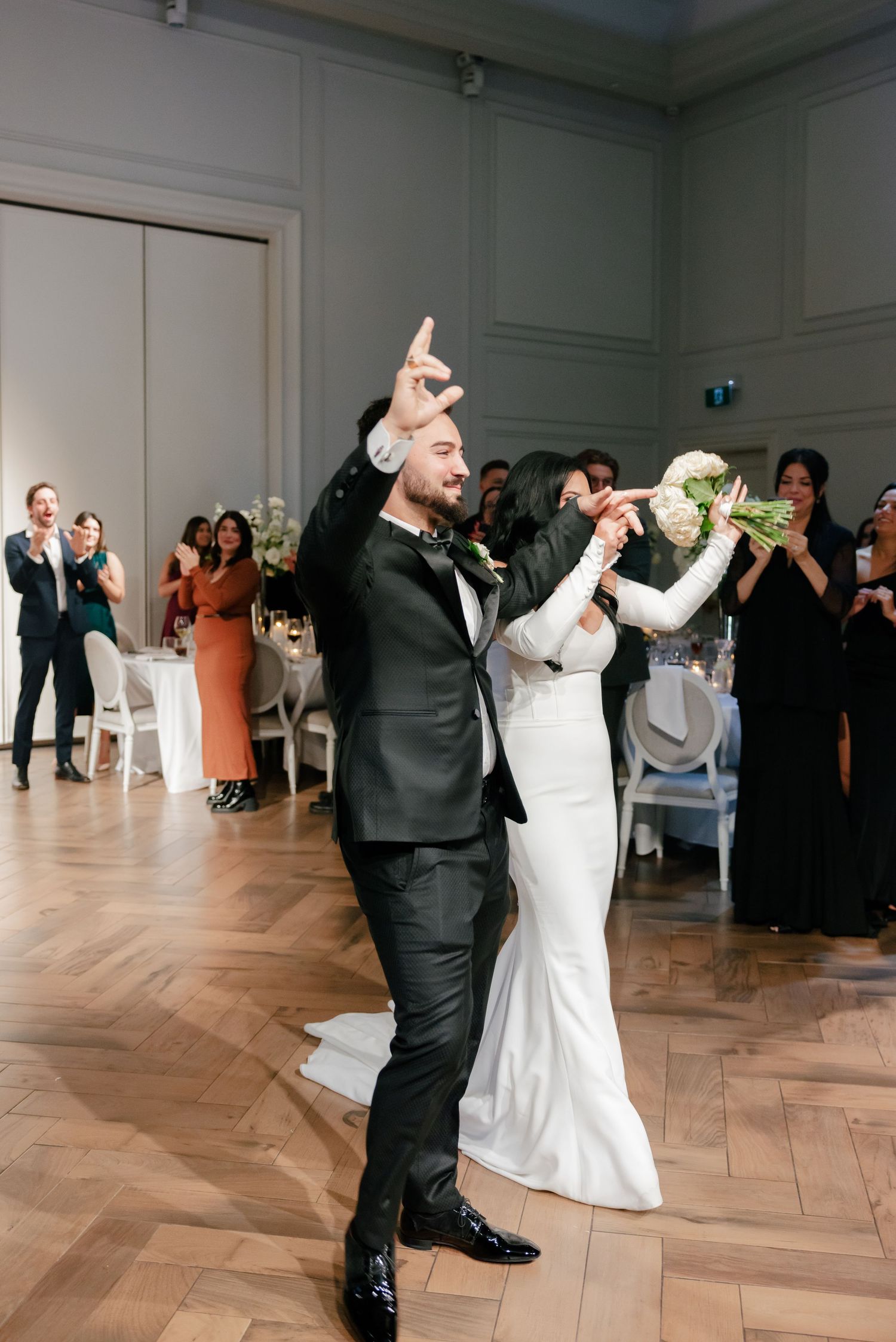 Celebratory moment during wedding reception with guests cheering in background.
