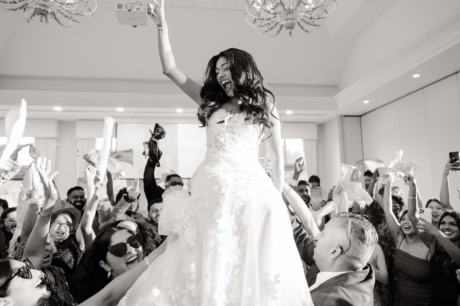 Black and white celebration shot with crowd cheering during wedding reception.