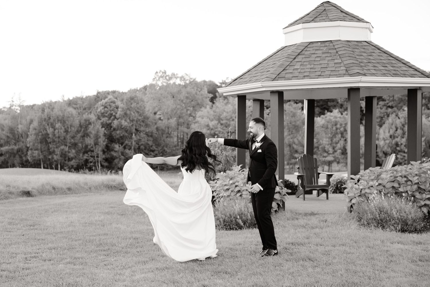 A black and white photo of newlyweds dancing beside their wedding gazebo.