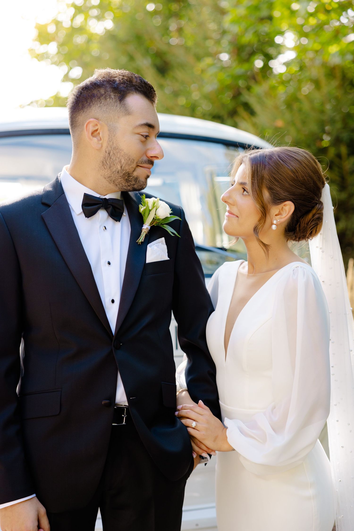 Joyful wedding couple sharing intimate moment next to vintage car in garden setting.