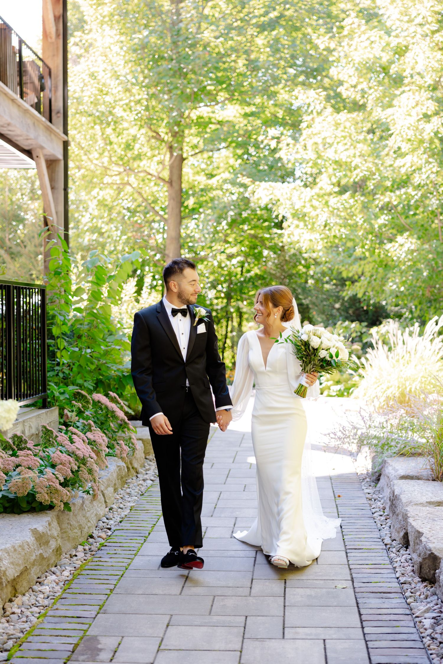 Wedding couple on stone pathway surrounded by garden landscaping and trees.
