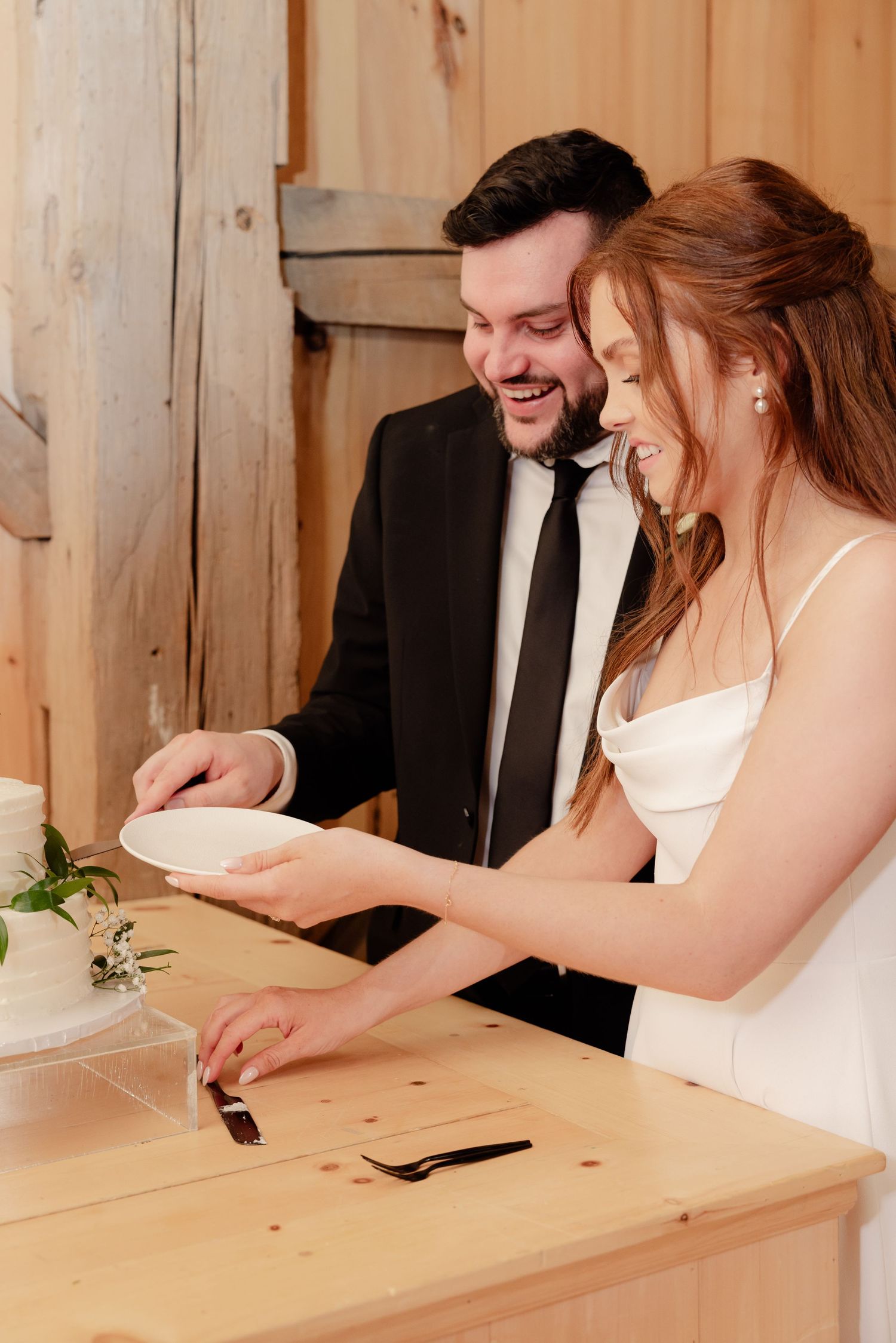 Wedding couple shares a joyful moment while cutting their wedding cake in a rustic wooden venue.