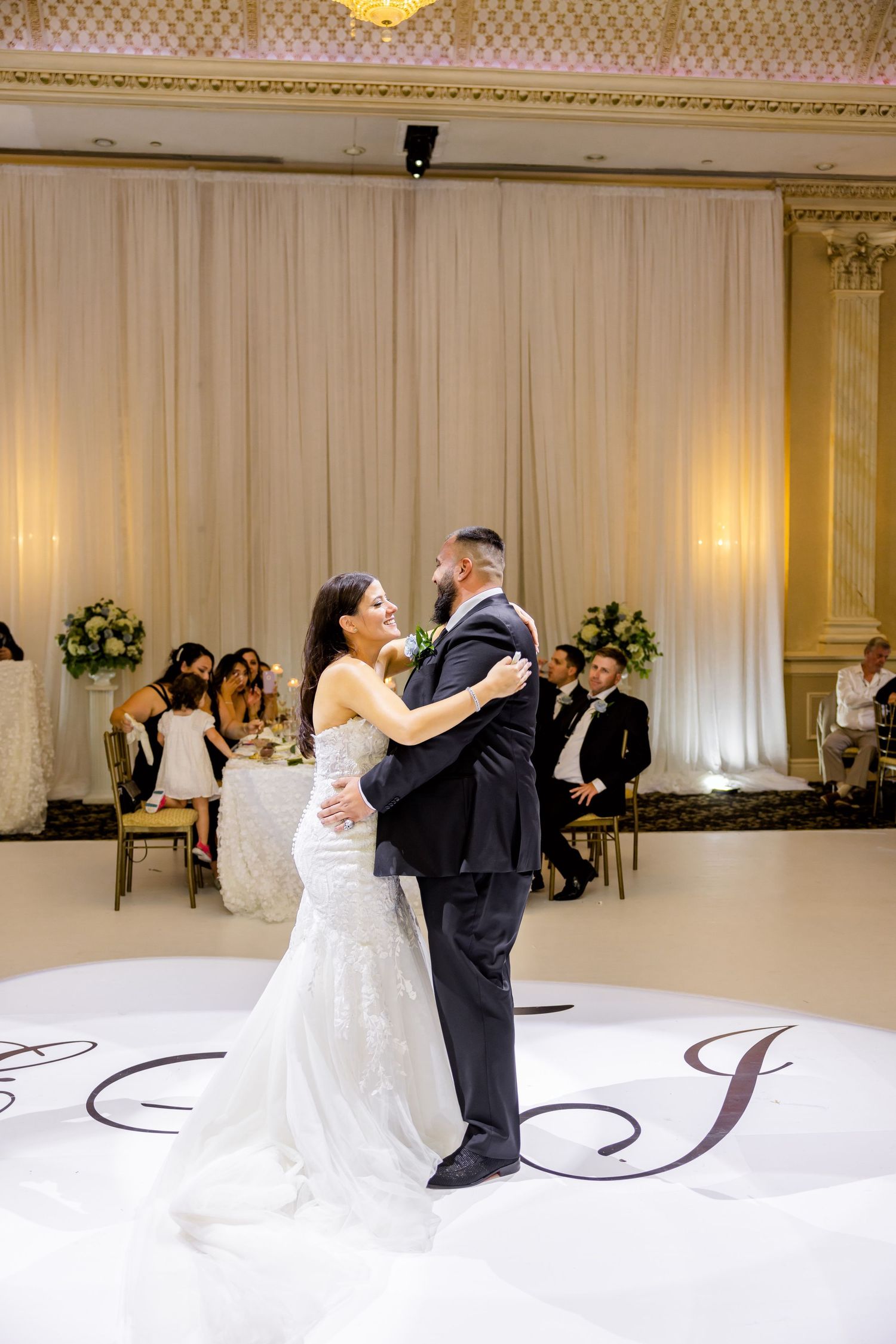 A couple shares their first dance on a monogrammed white dance floor at their wedding reception.