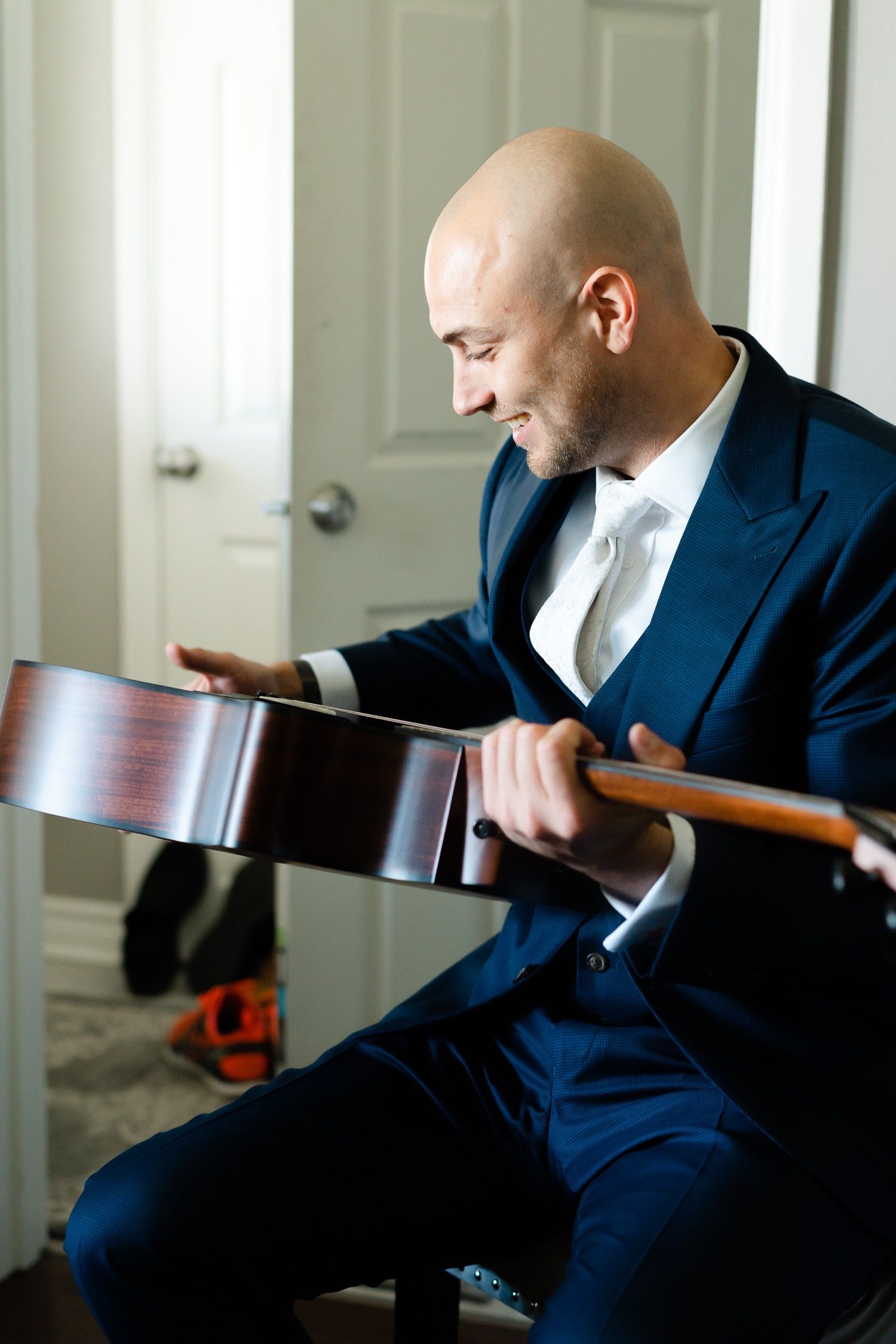 Person in navy blue suit sits indoors examining a wooden guitar or instrument.