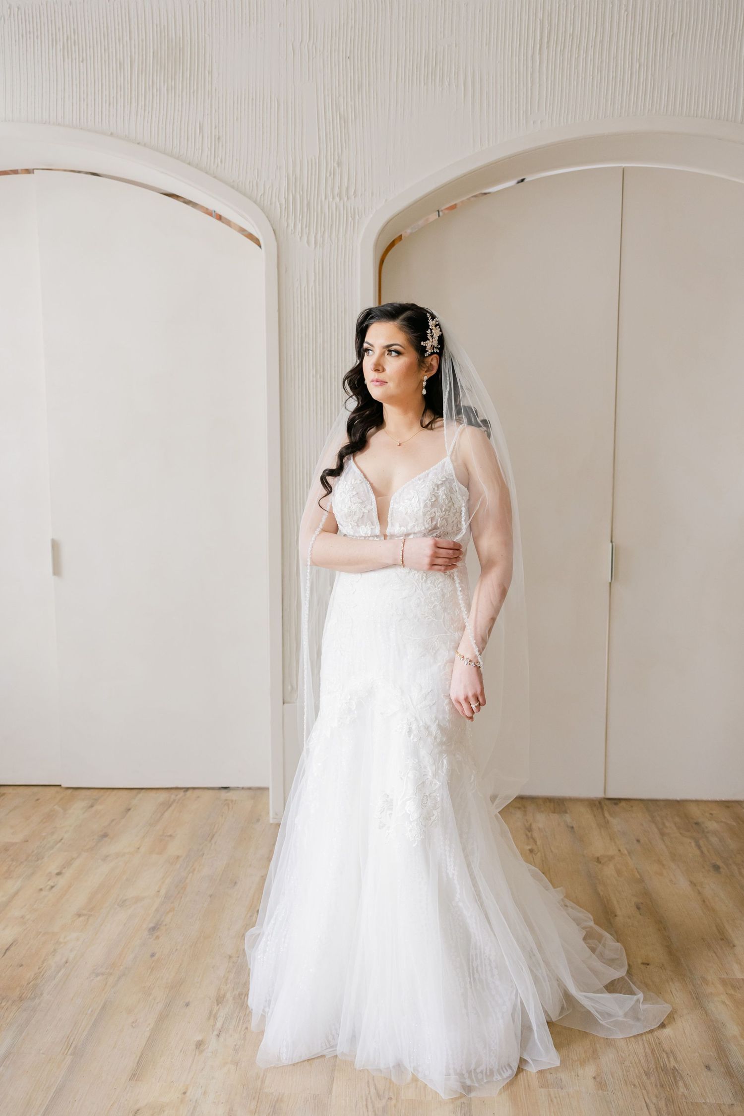 Full length bridal portrait showing a fitted lace wedding gown against a light backdrop.