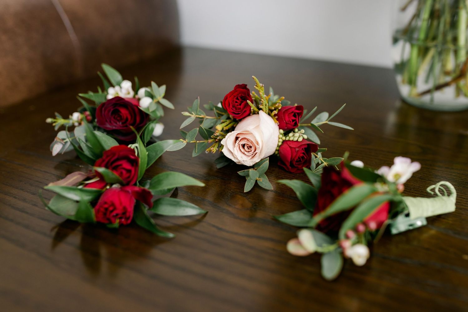 Red and blush rose boutonnieres with eucalyptus arranged on wooden surface.