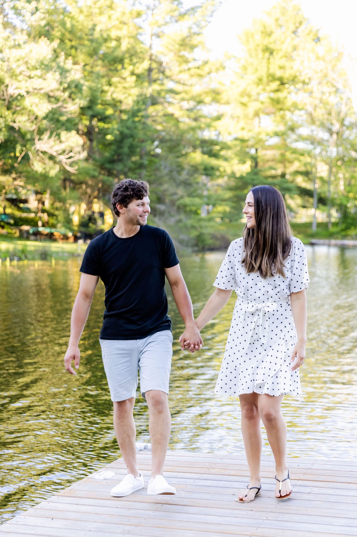 Couple walking hand in hand on lakeside dock wearing casual summer clothes.