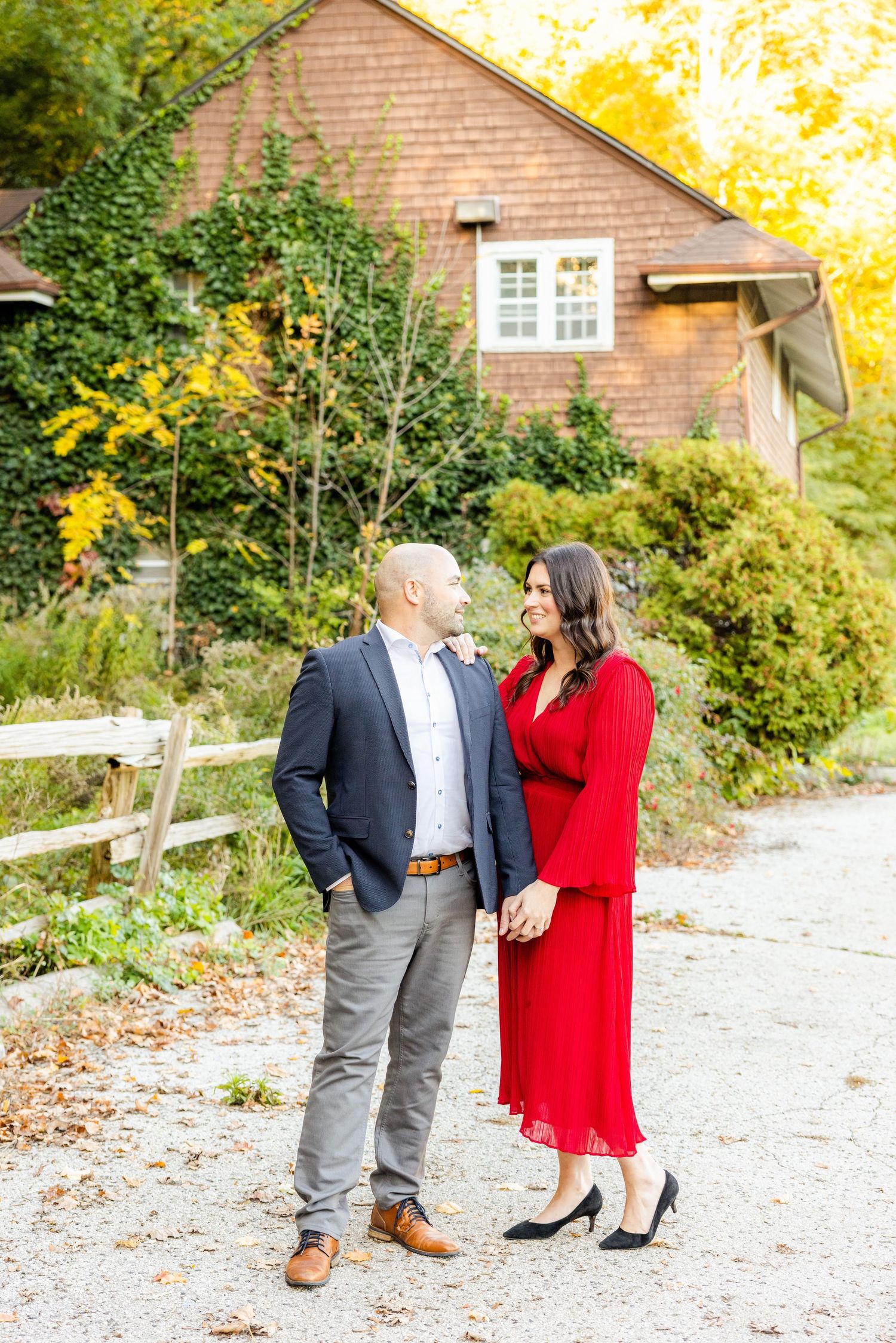 Romantic couple share a moment outside brown cottage with autumn trees in background.