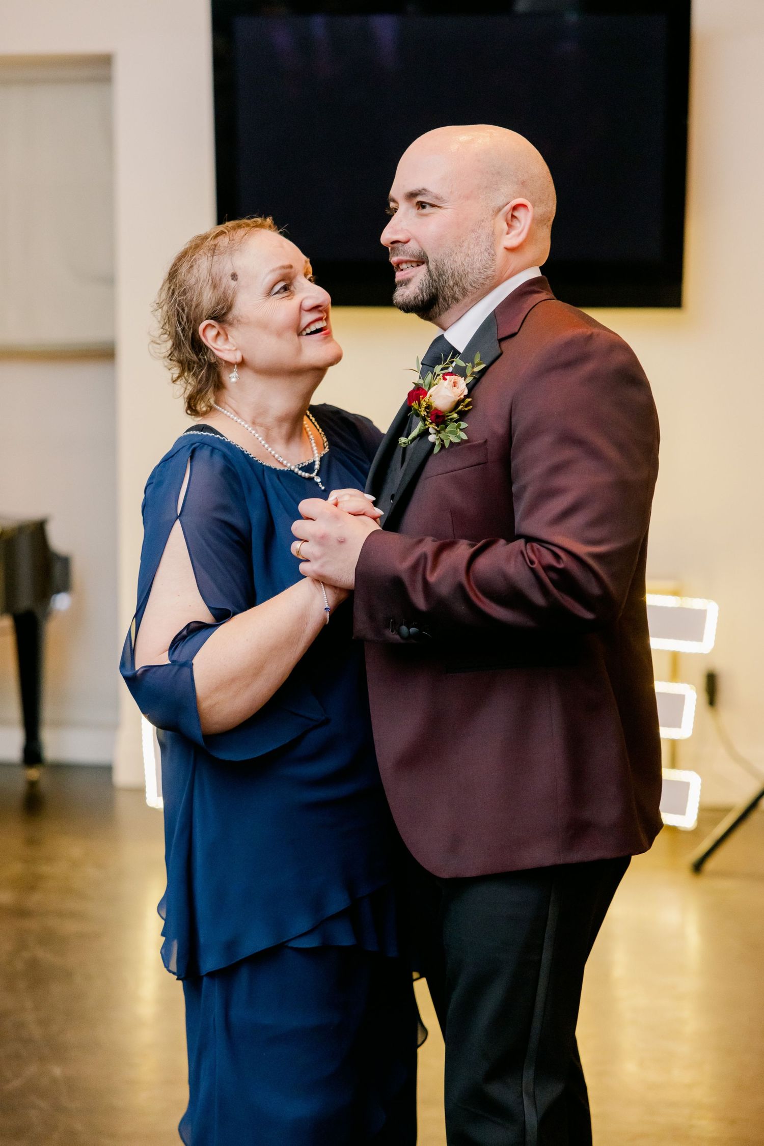 A couple dances together at a wedding, with the woman in navy blue and man in burgundy suit.