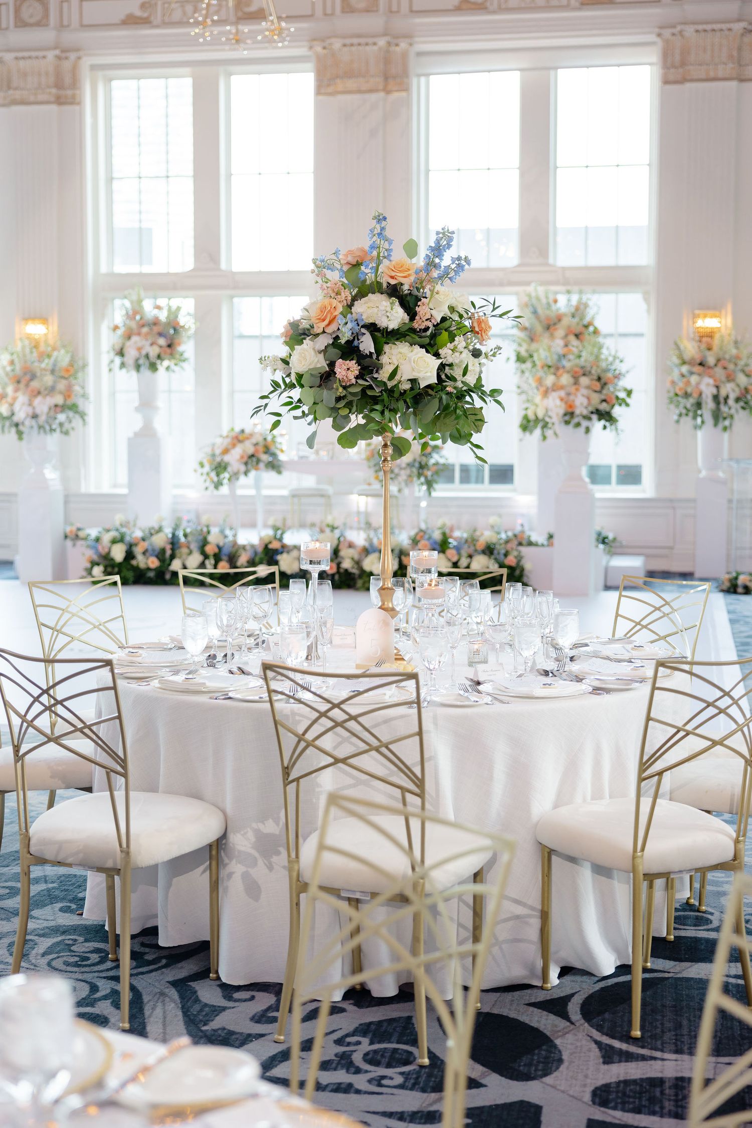 Elegant wedding reception tables with white linens, gold chairs, and lush floral centerpieces.