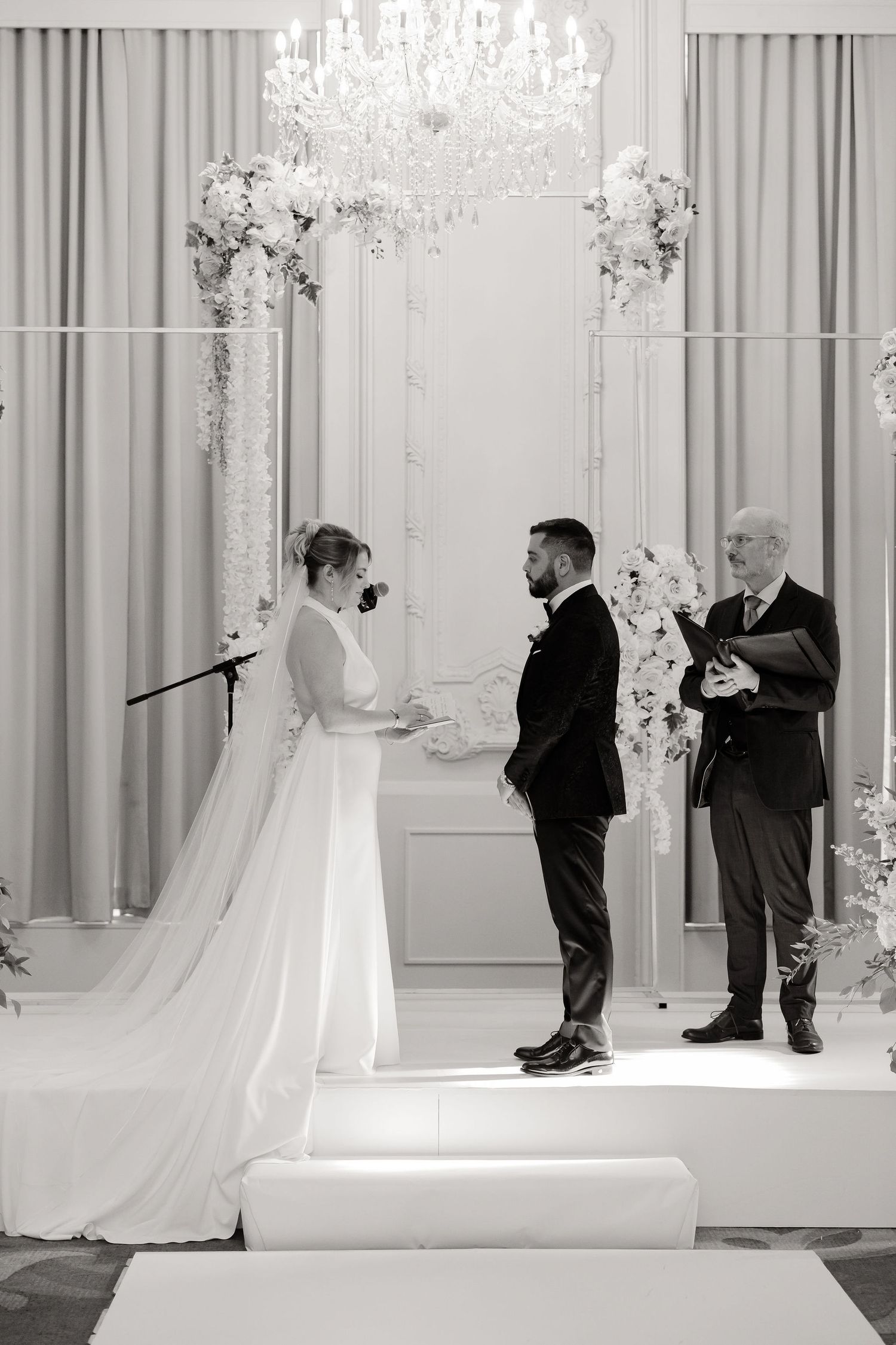 Wedding ceremony setup showing photographers and staff preparing in an elegant white room with chandeliers.