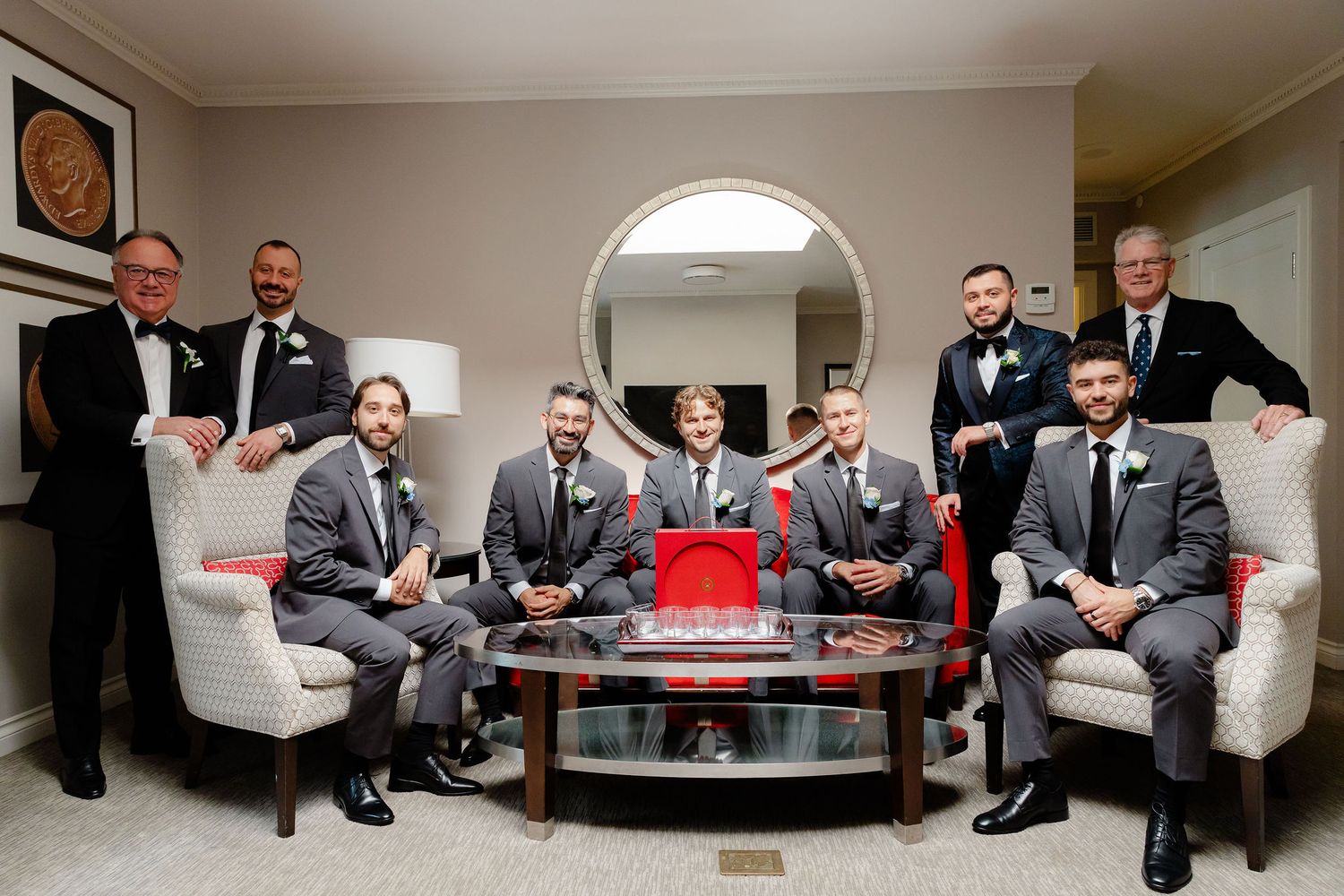A wedding party in formal attire gathers on a white couch around a coffee table.
