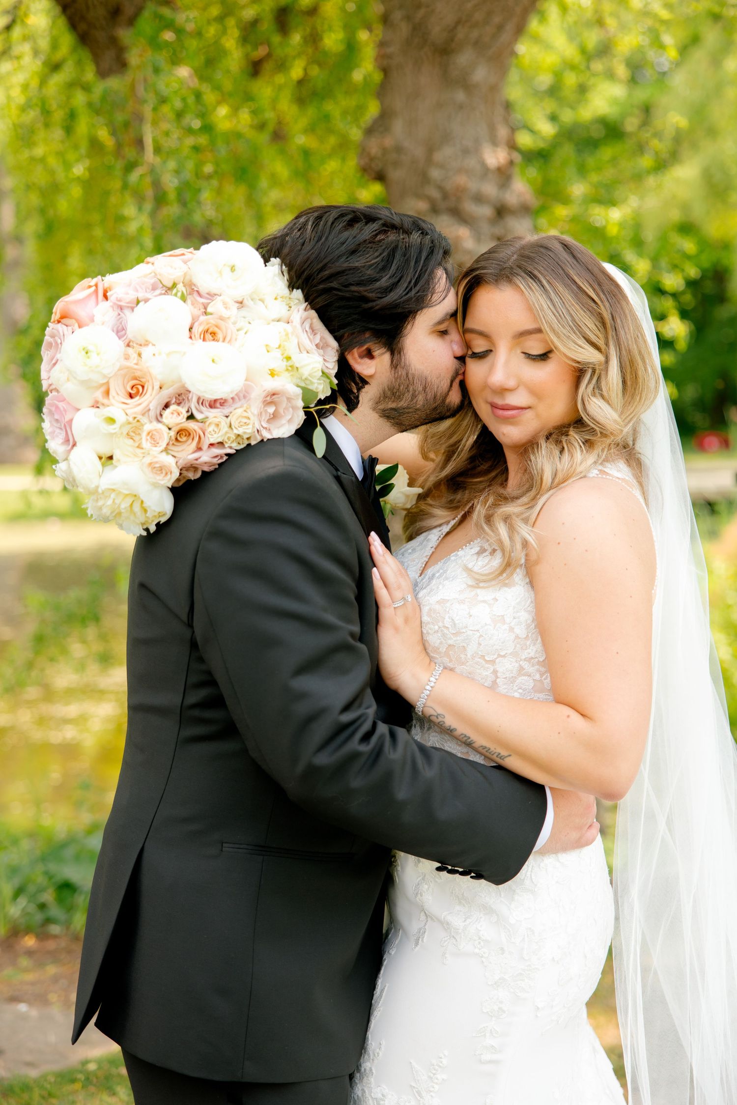 Romantic wedding moment with a lush blush pink bouquet under a tree in a garden setting.