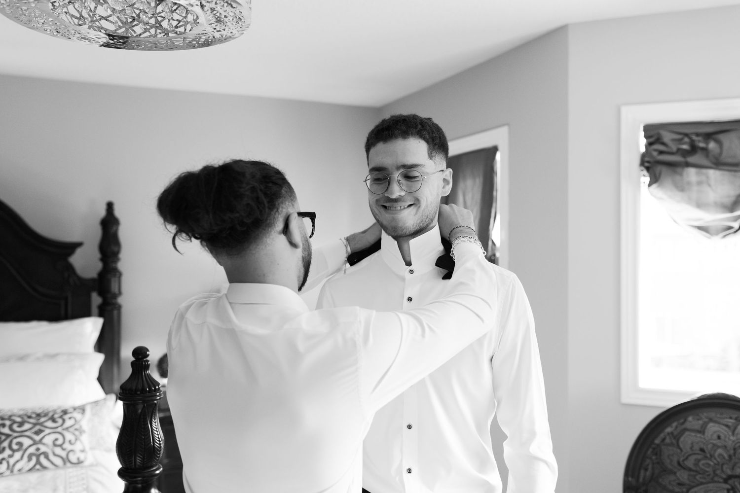 Two formal-dressed people assisting with clothing adjustments in a bedroom.